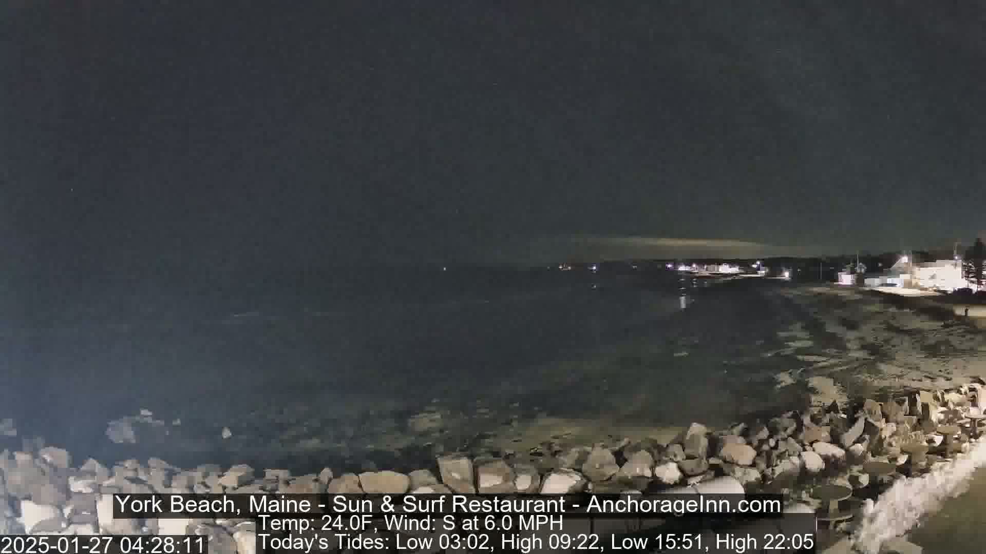 A nighttime view of a rocky shoreline and dark ocean under a clear, dark sky.