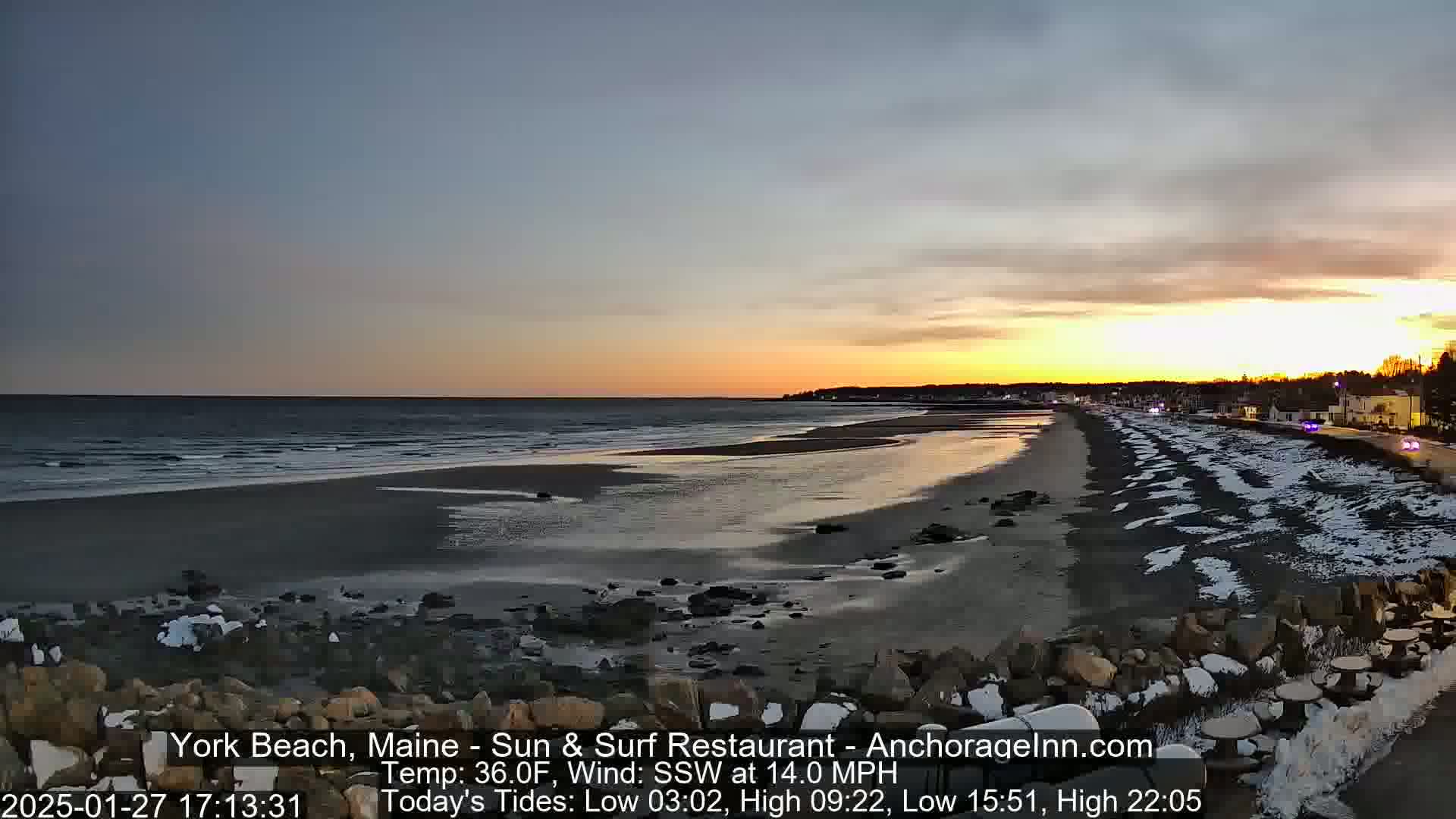 A partly cloudy sunset over a snow-dusted beach with a calm ocean.