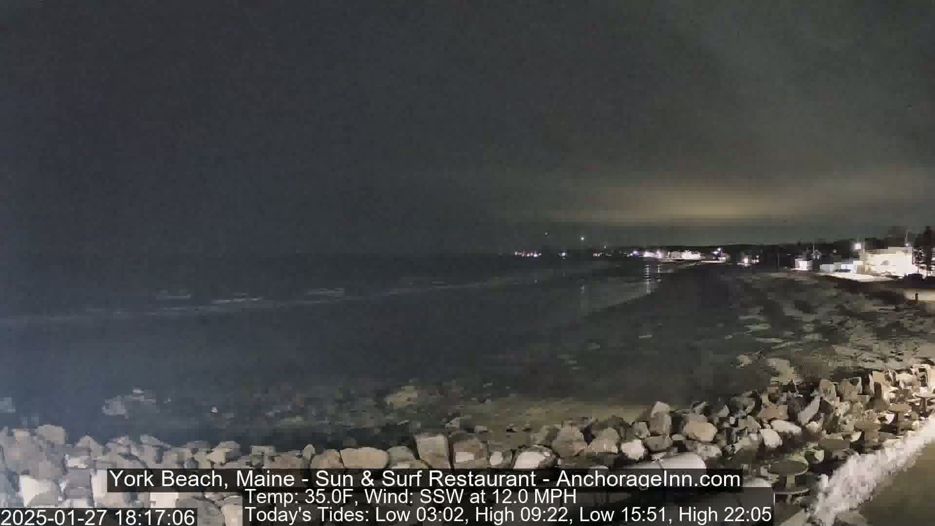 A nighttime view of a rocky shoreline and dark ocean under a cloudy sky.