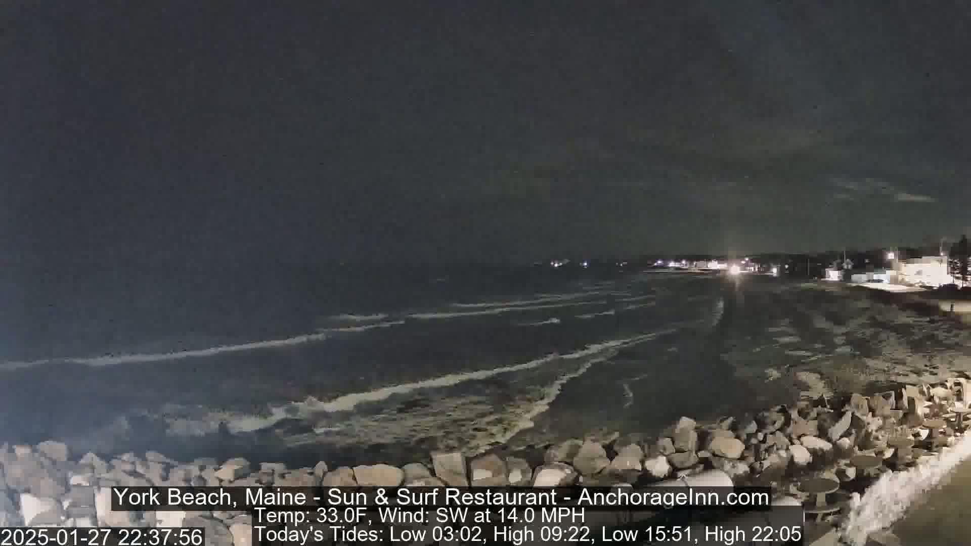 A nighttime view of a rocky shoreline with moderately rough waves under a dark sky.