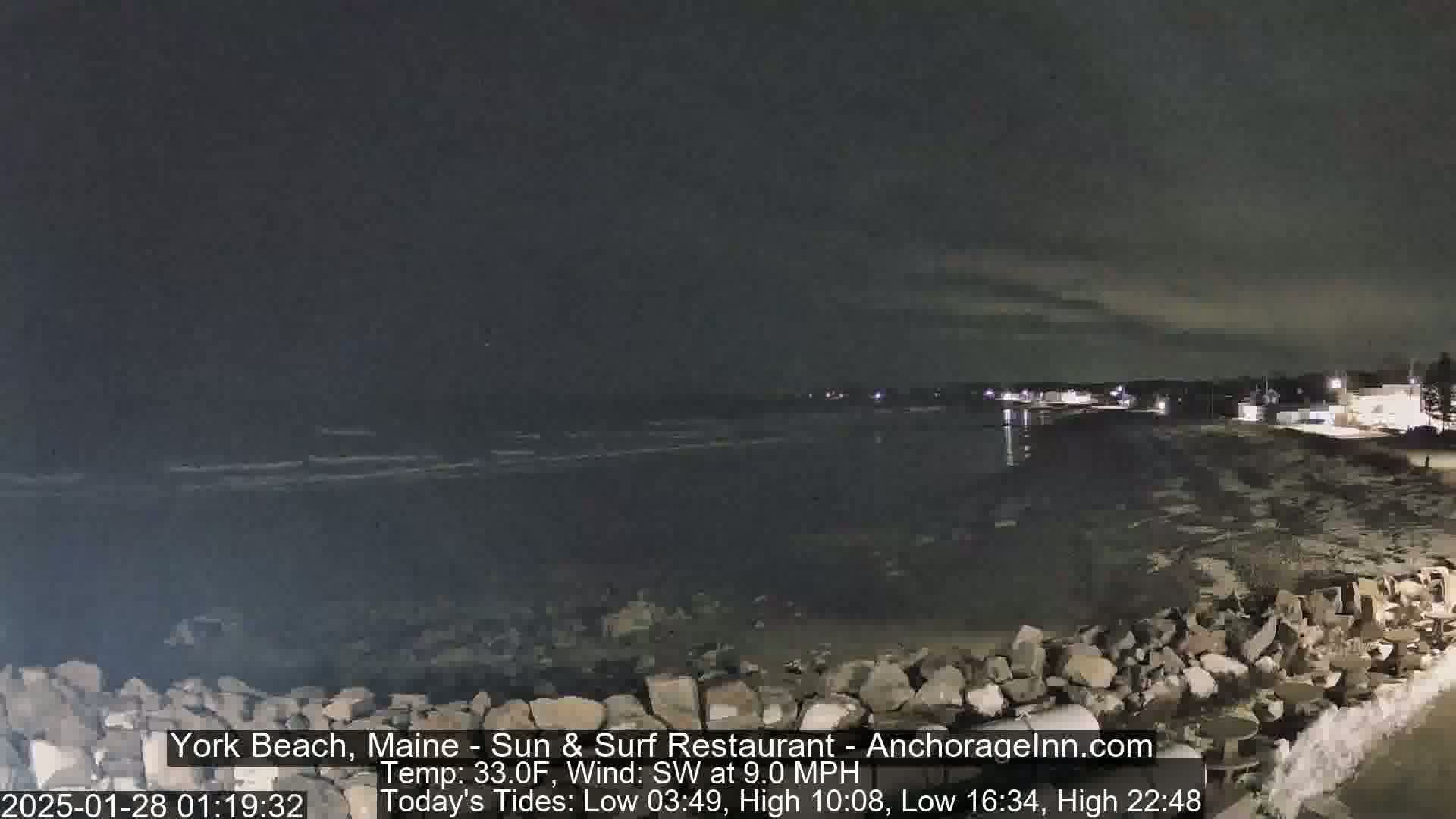 A nighttime view of a rocky shoreline and dark ocean under a cloudy sky.