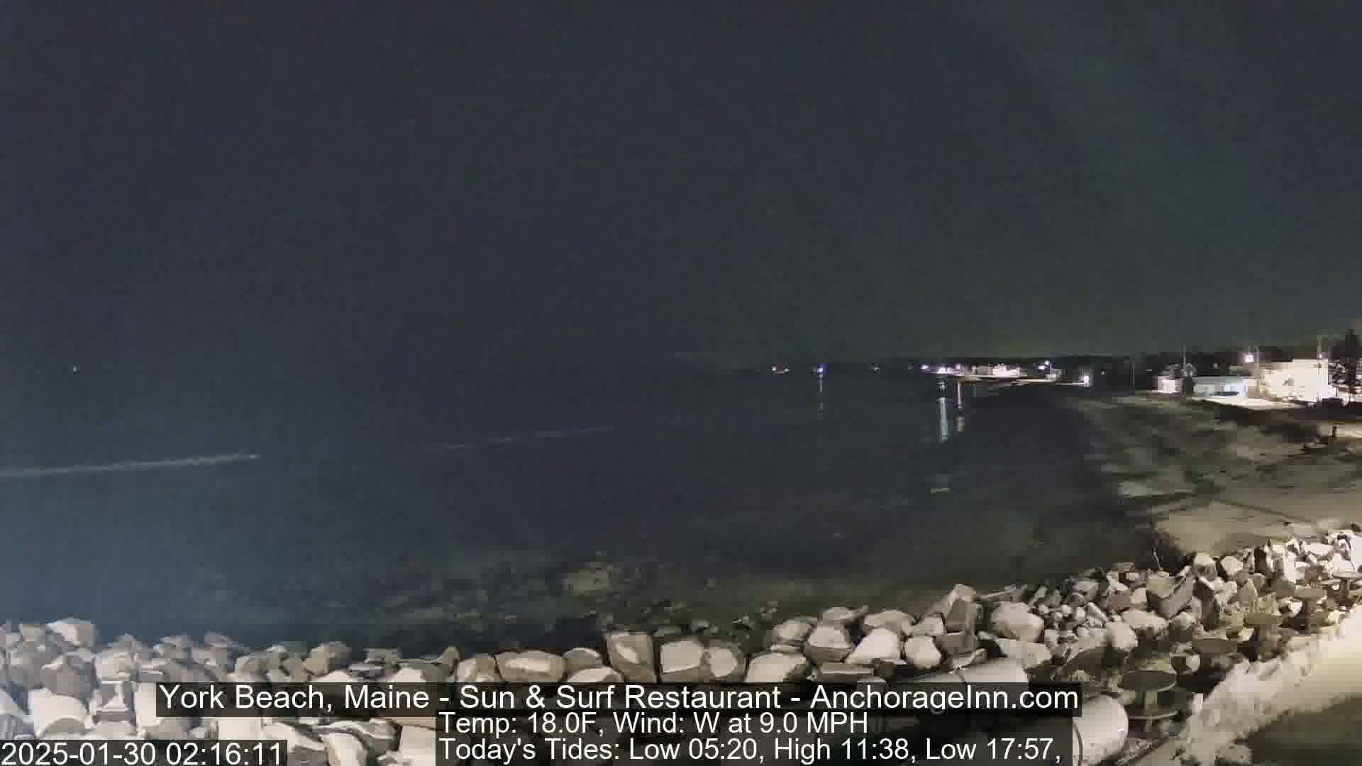 A nighttime view of a dark, rocky shoreline and calm ocean under a clear sky.