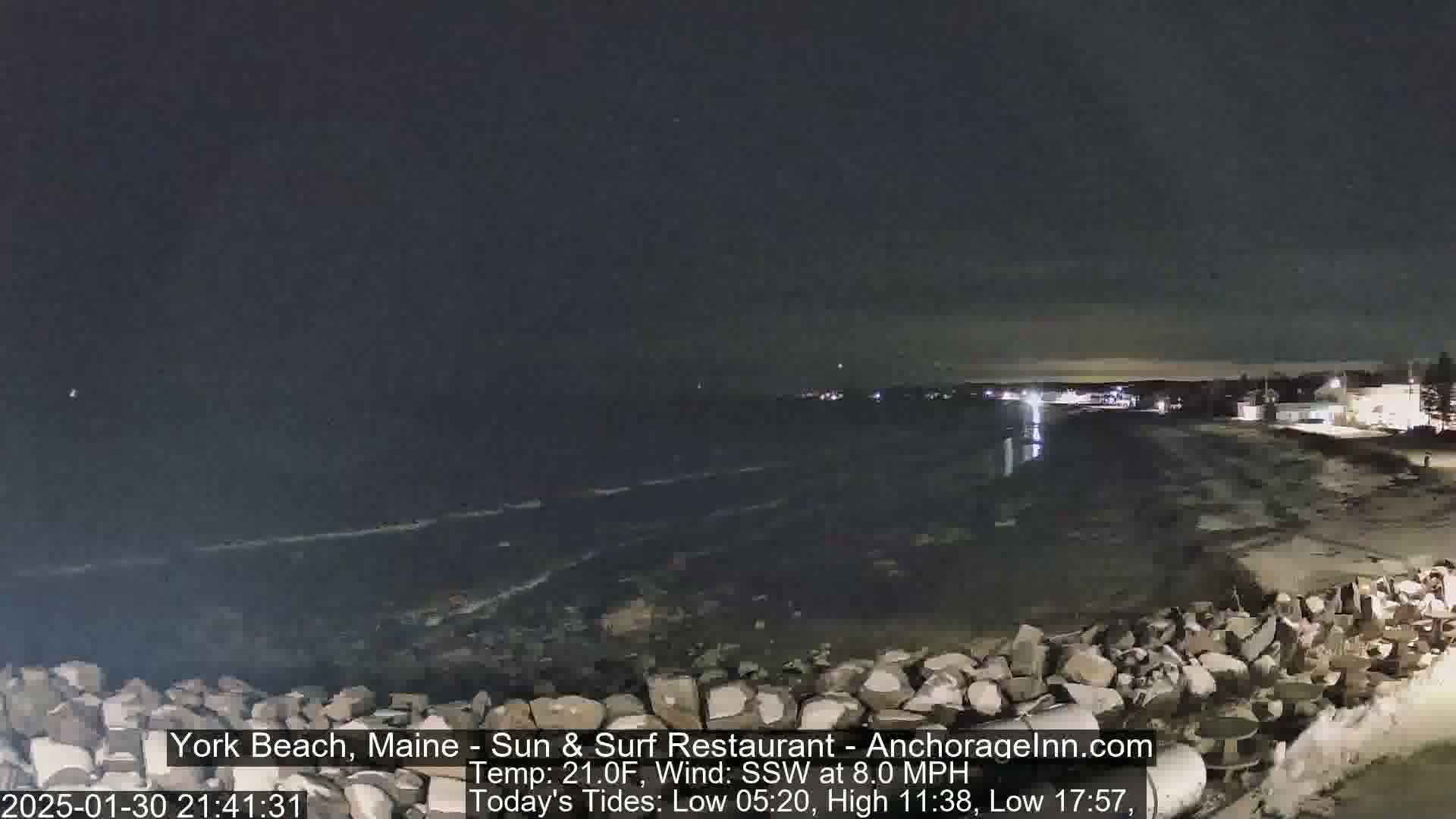 A nighttime view of a rocky shoreline and dark ocean under a clear sky, with gentle waves.