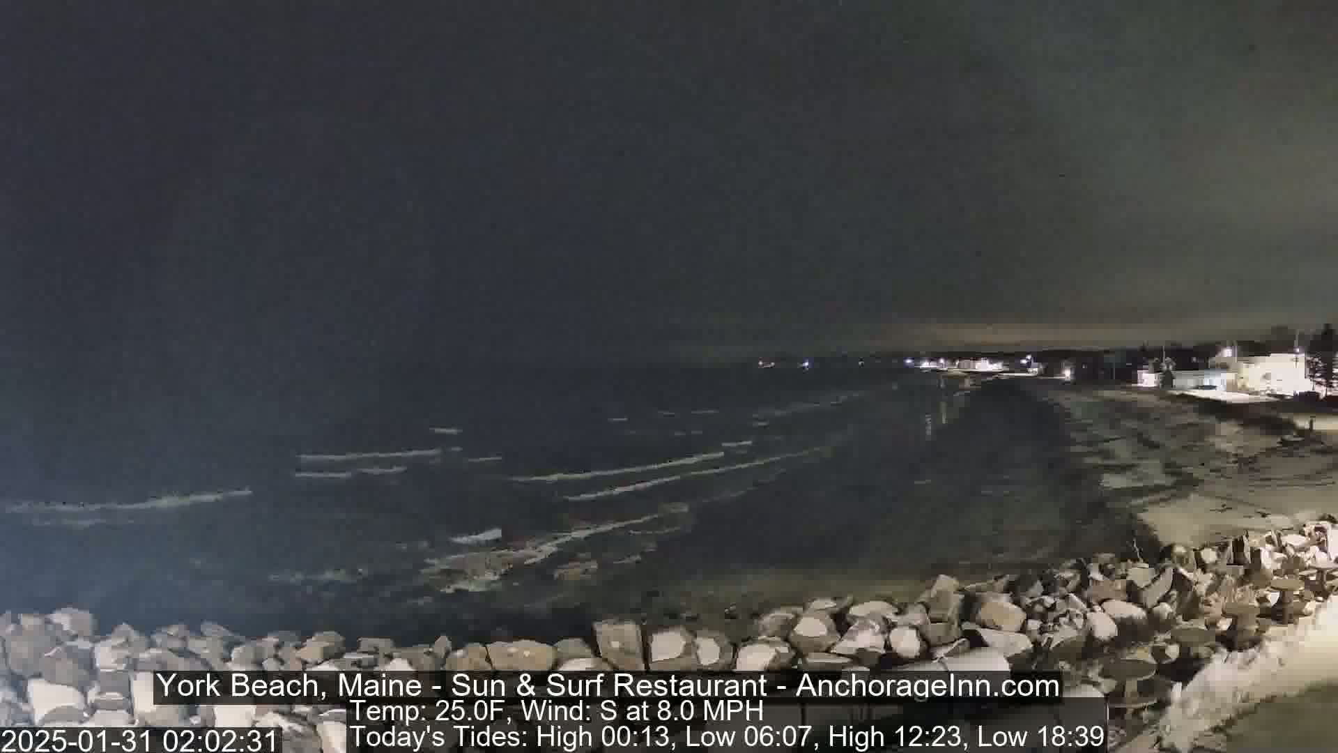 A nighttime view of a rocky shoreline and dark ocean with small waves under a dark sky.