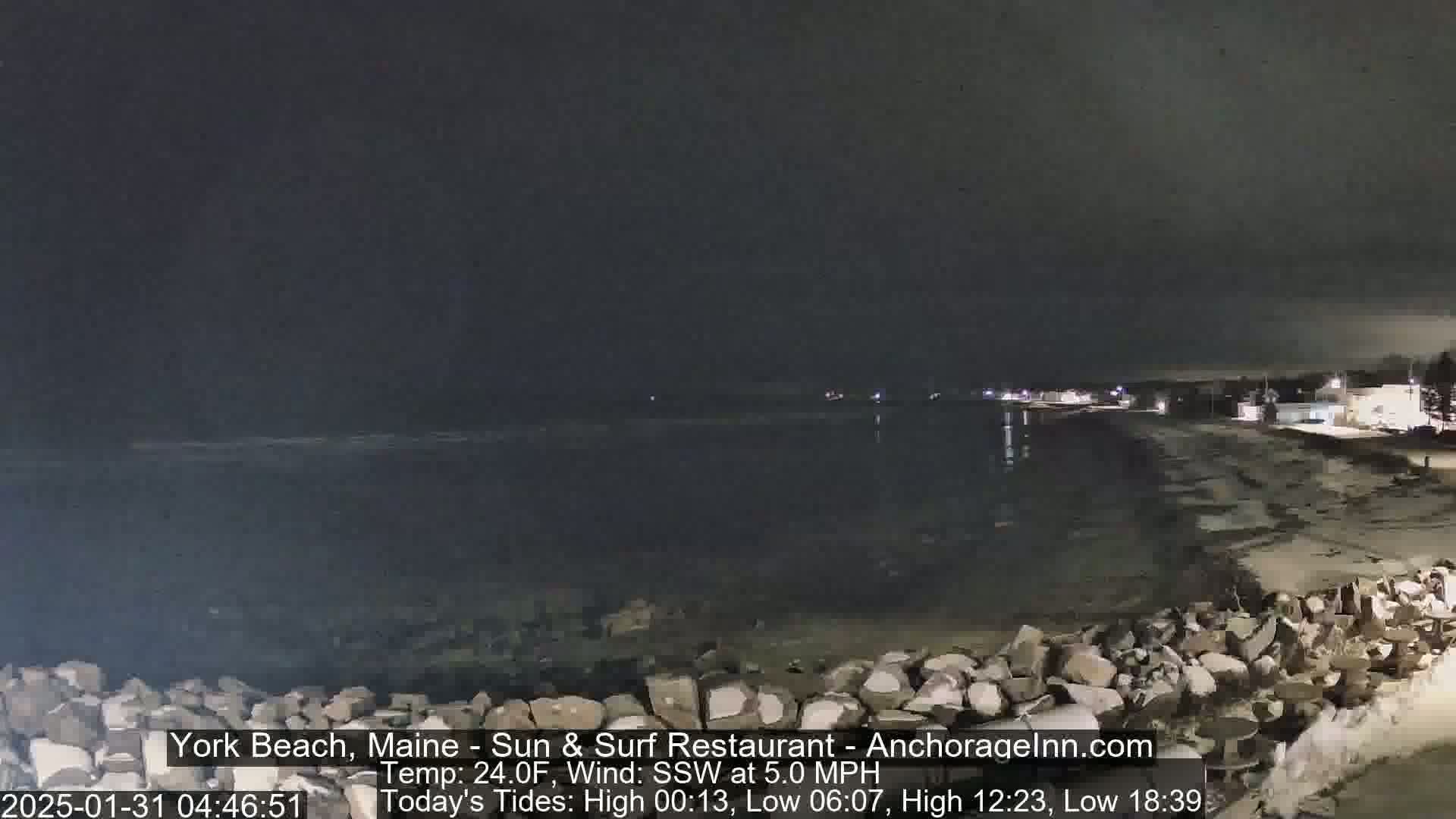 A nighttime view of a rocky shoreline and calm ocean under a dark sky.