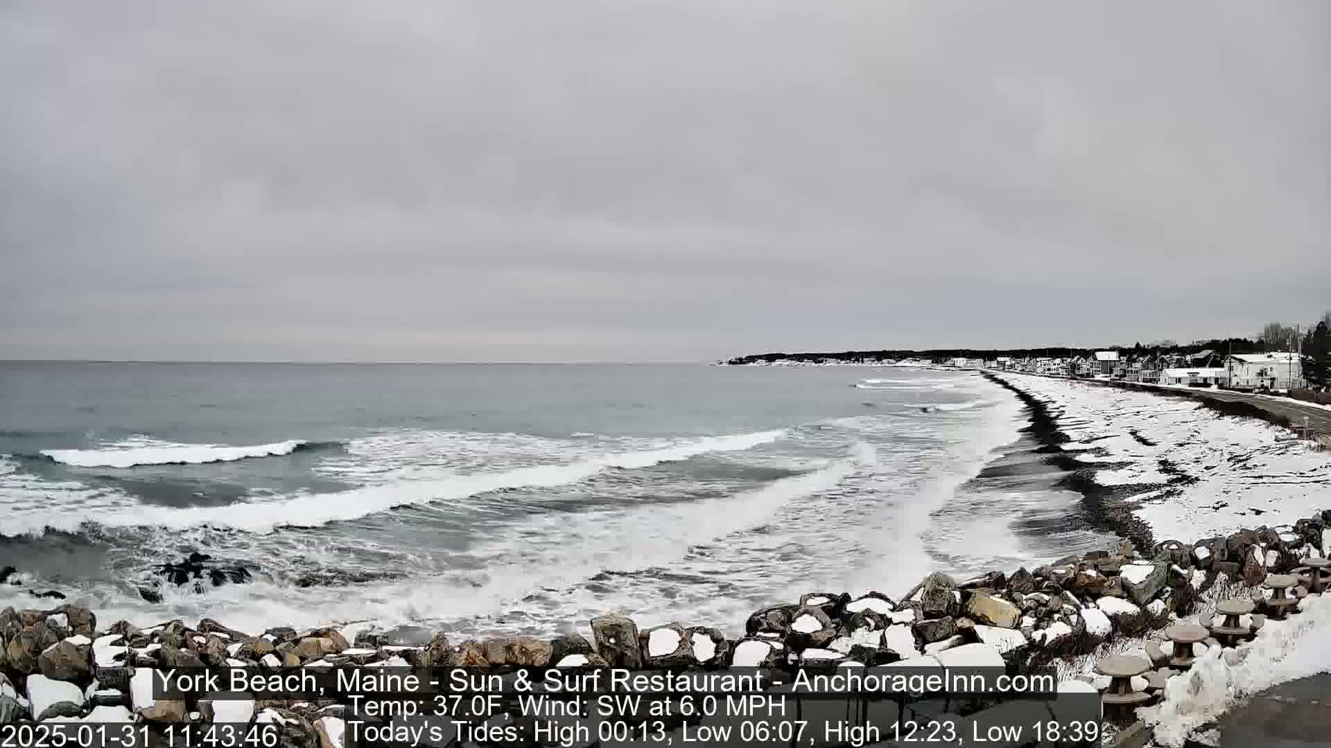 A snow-dusted rocky shoreline meets a gray ocean with small waves under an overcast sky.