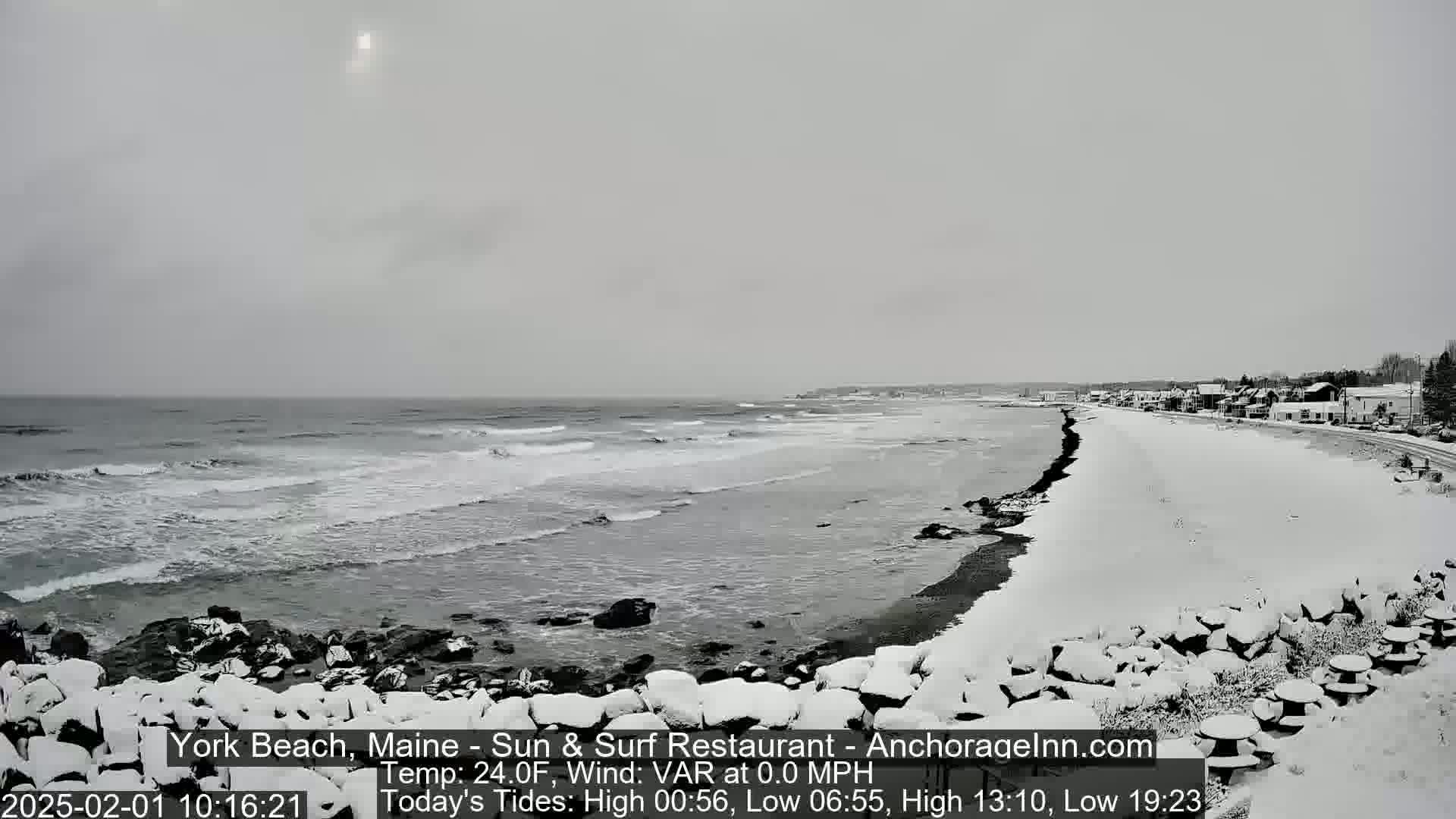 A snow-covered beach with a calm ocean under an overcast sky.