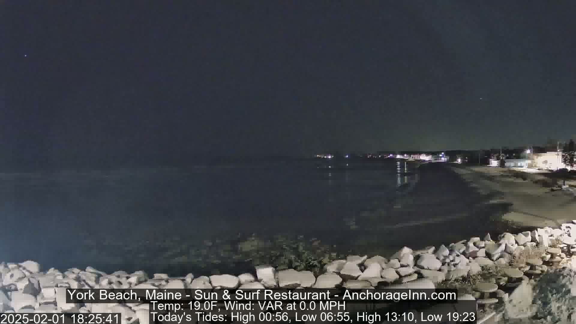 A nighttime view of a rocky shoreline and calm ocean under a dark, clear sky.