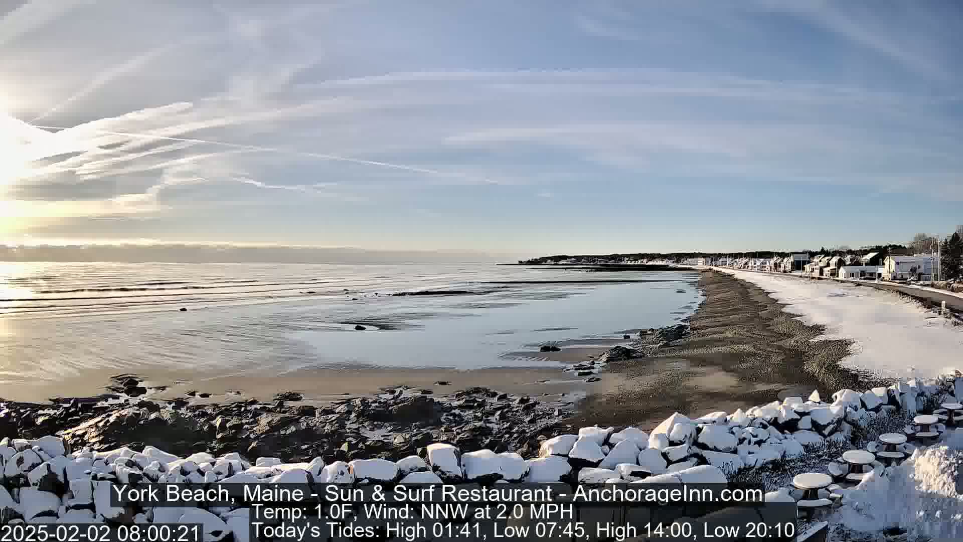 A snow-dusted beach stretches along a calm ocean under a partly sunny sky.