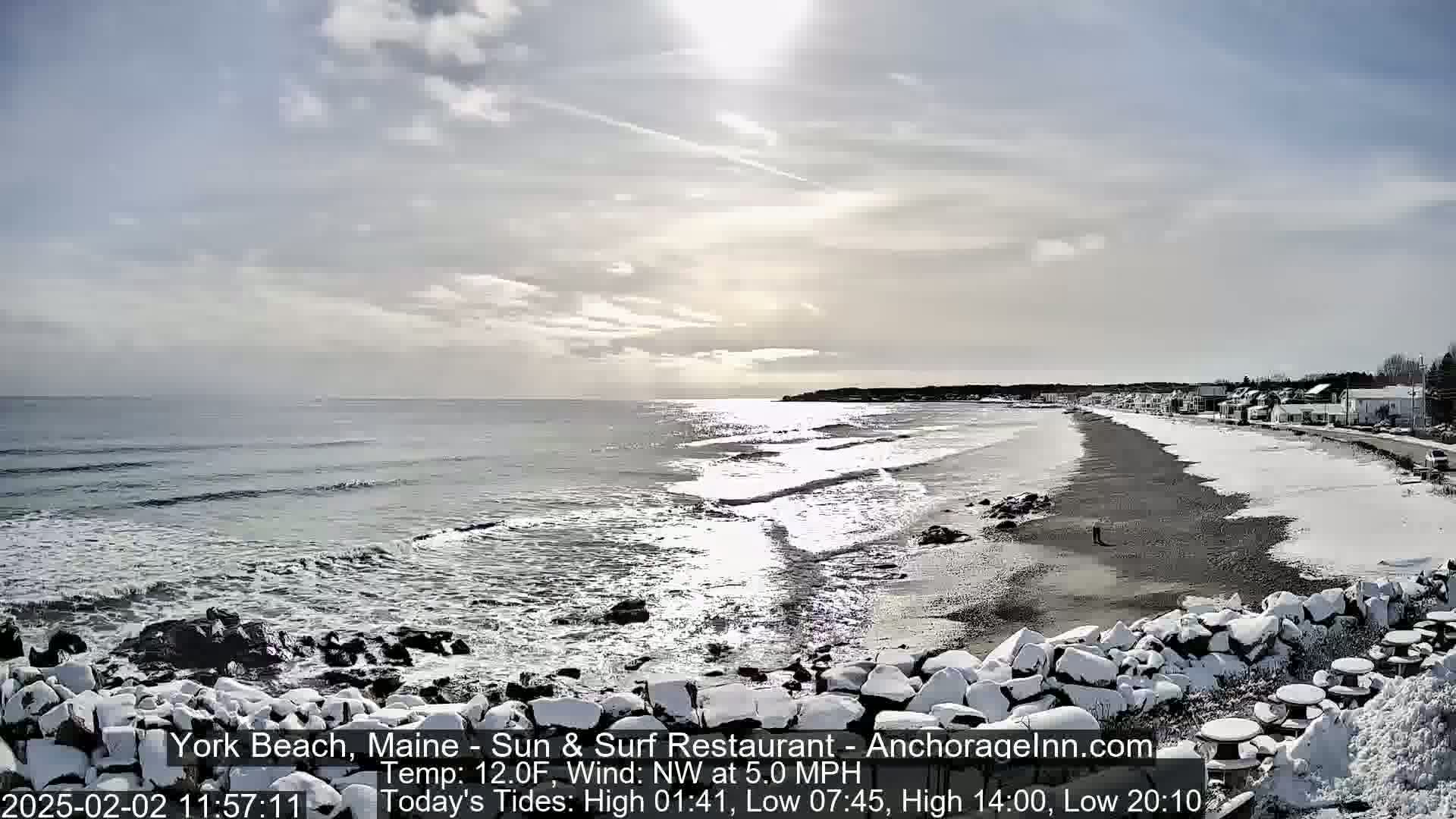 A snow-covered beach with a partly sunny sky and waves crashing on the shore.
