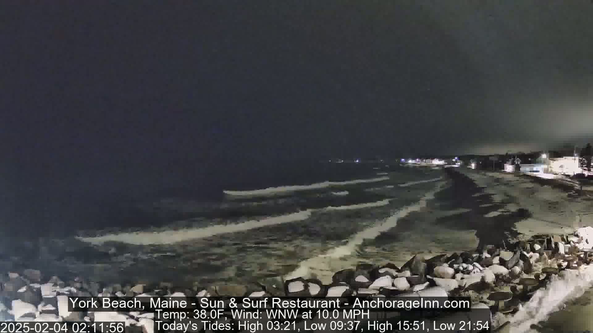 A nighttime view of a rocky shoreline with waves breaking against it under a dark sky.