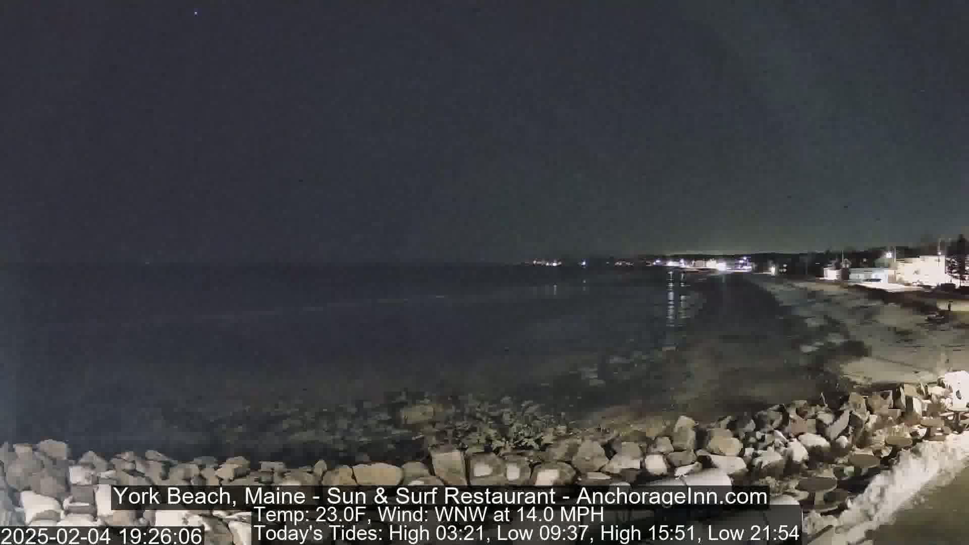 A nighttime view of a dark, rocky shoreline and calm ocean under a clear, dark sky.