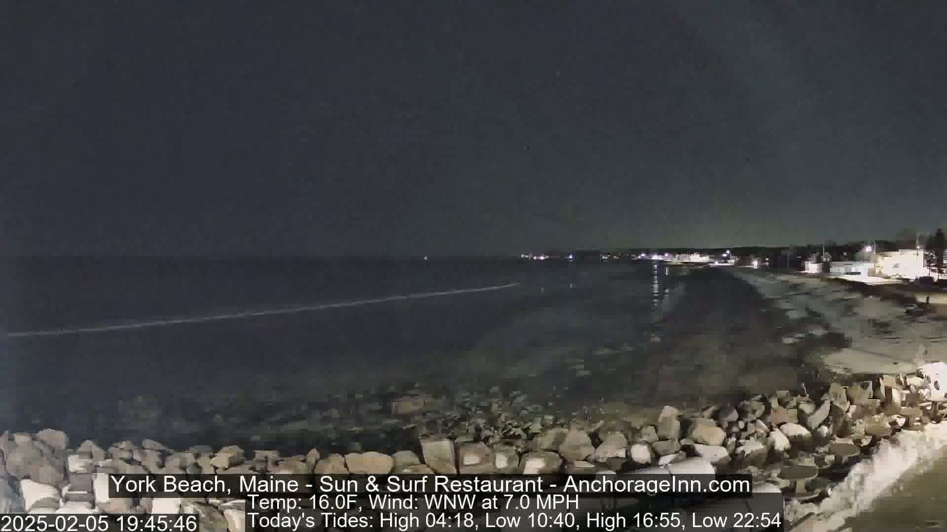 A nighttime view of a rocky shoreline and dark ocean under a clear, dark sky.