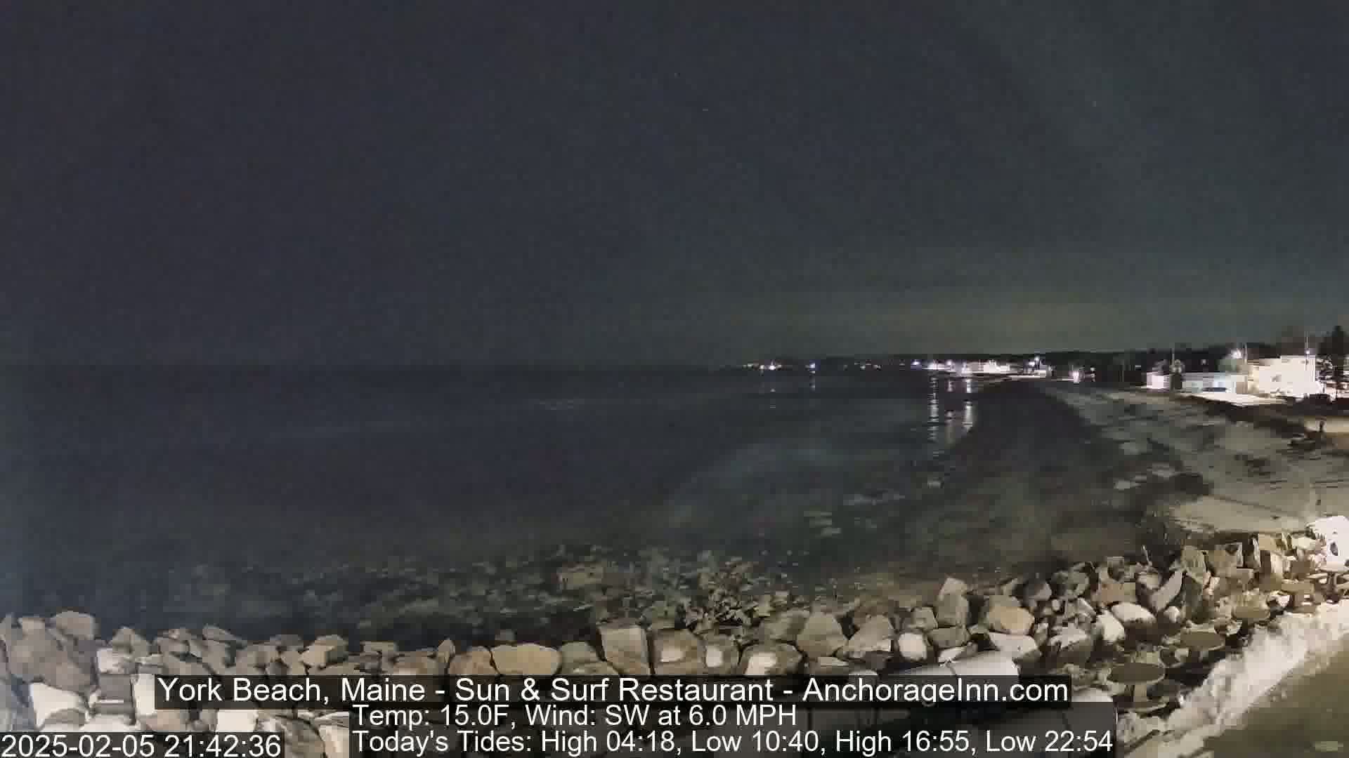 A nighttime view of a rocky shoreline and calm ocean under a dark sky.