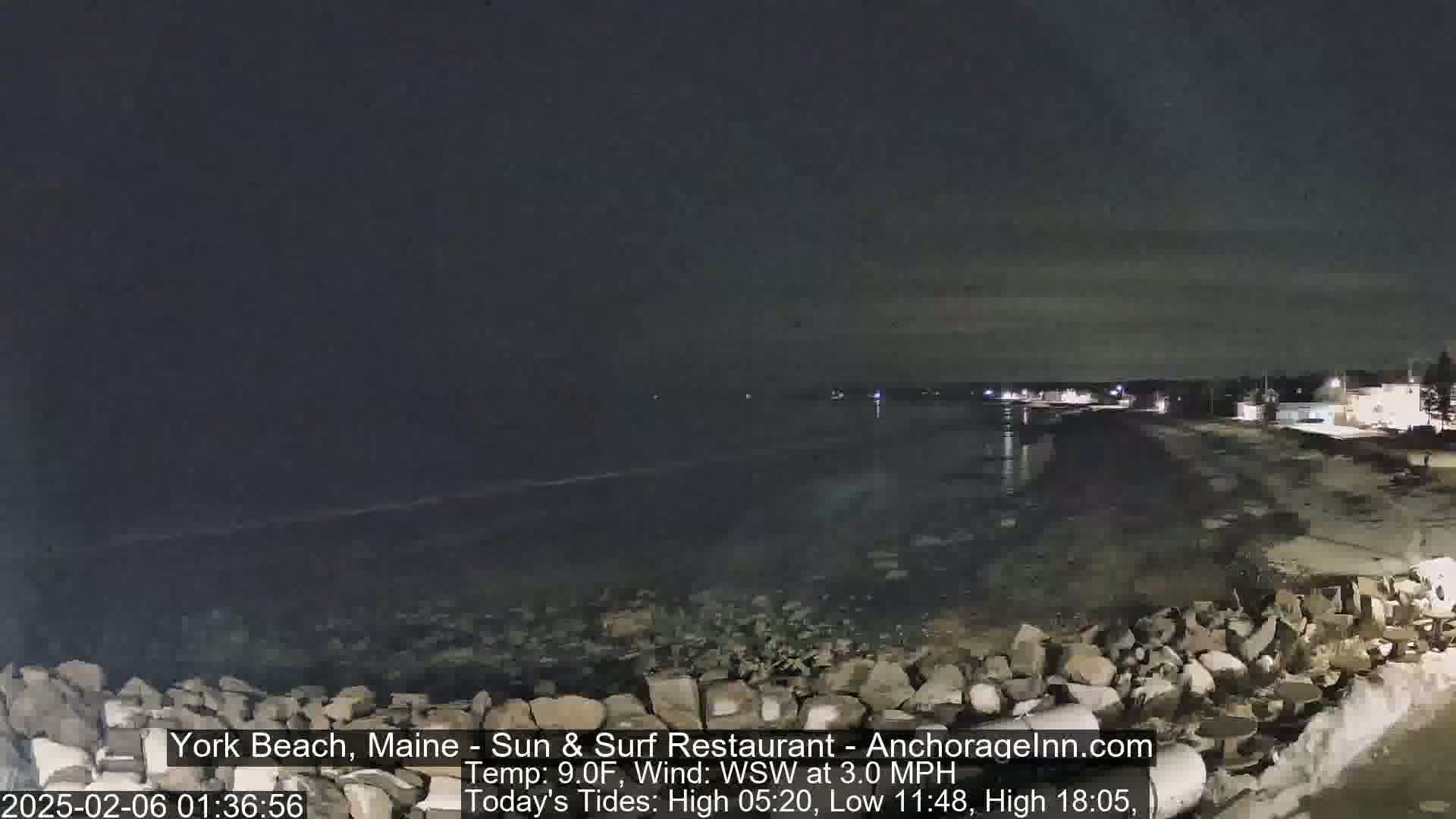A nighttime view of a dark, rocky shoreline and calm ocean under a mostly clear sky.