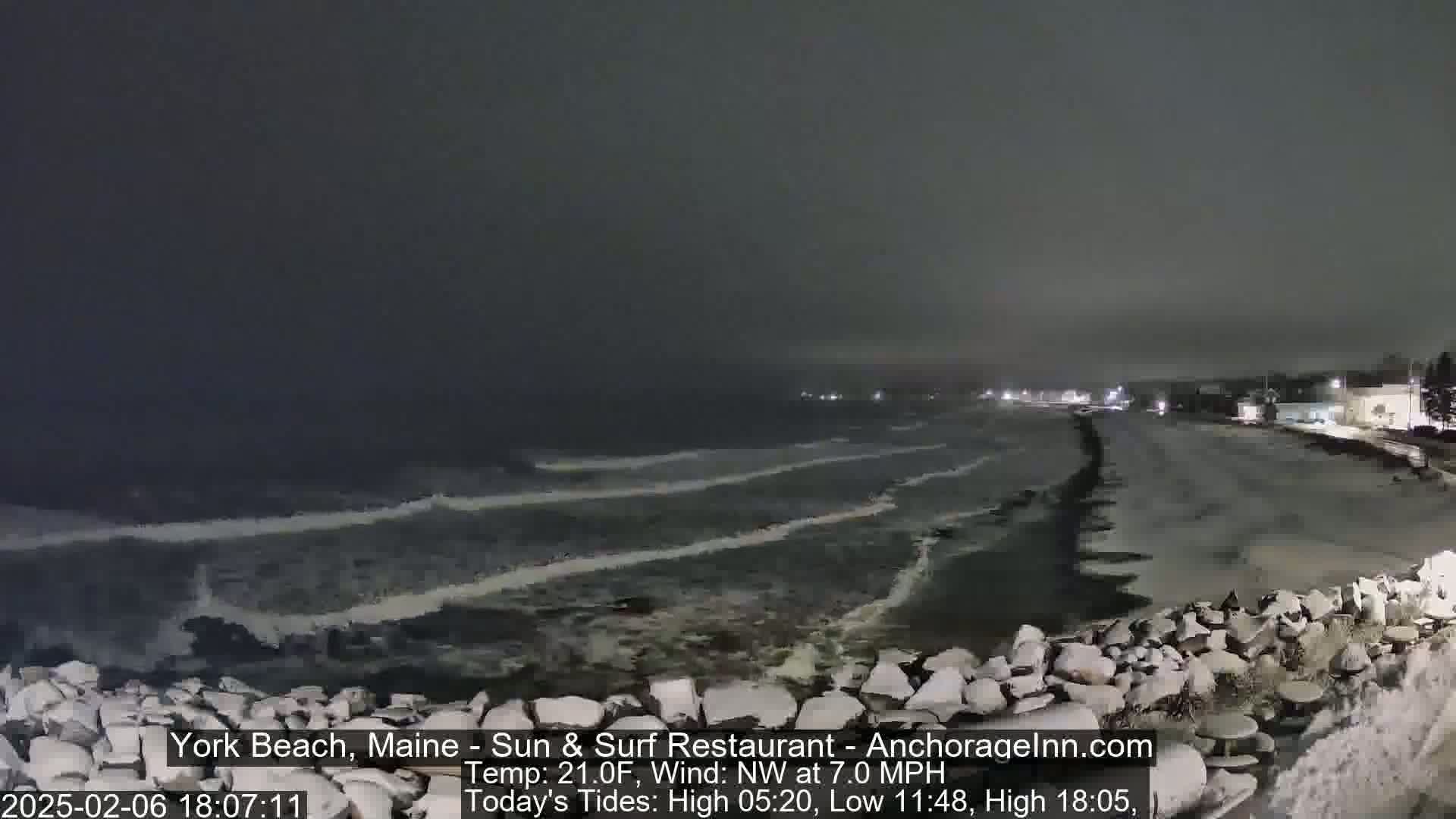 A nighttime view of a rocky shoreline with dark, wavy water under a gray sky.