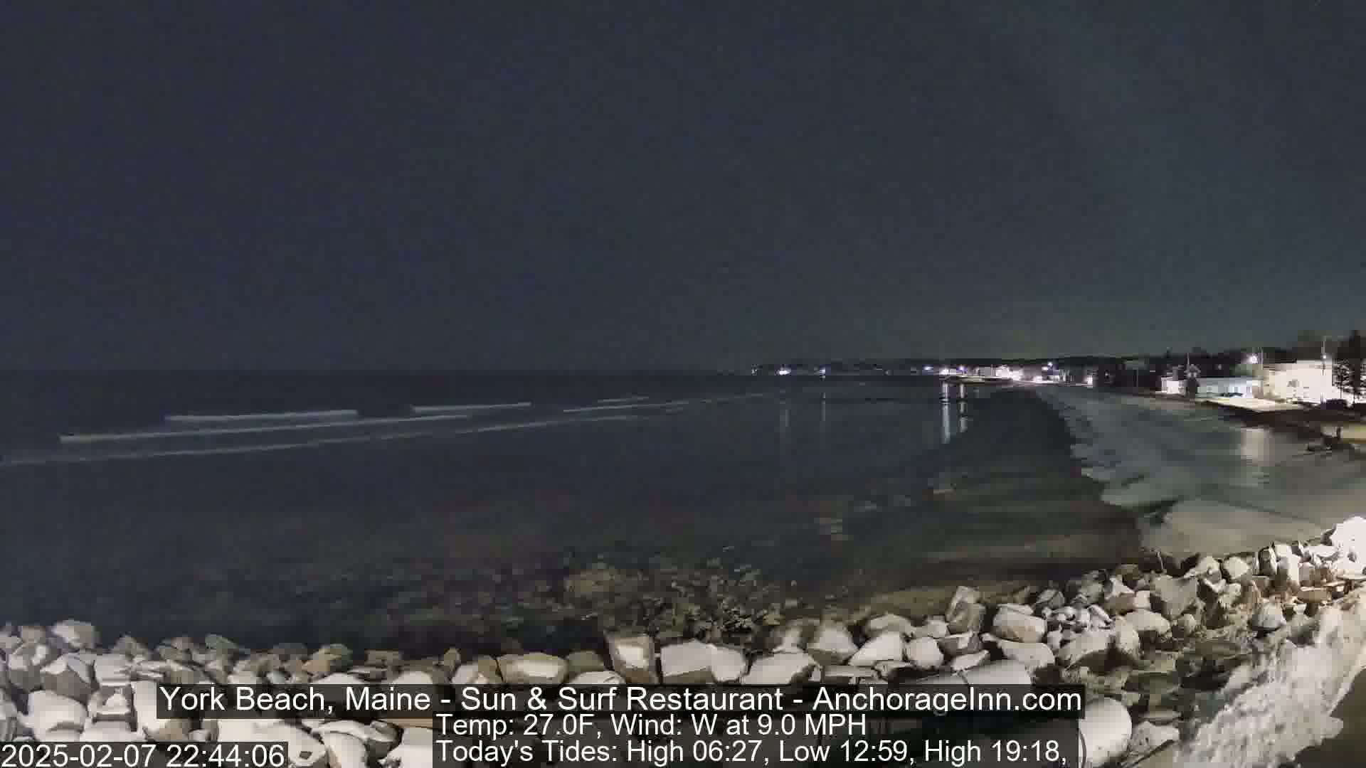 A nighttime view of a rocky shoreline with a calm ocean under a dark sky.