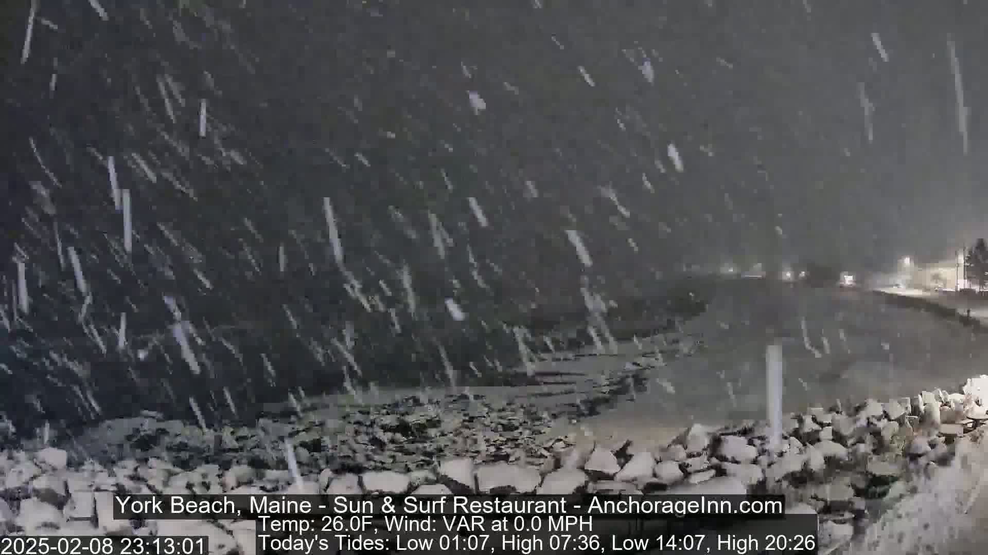 A nighttime scene of heavy snowfall over a rocky shoreline.