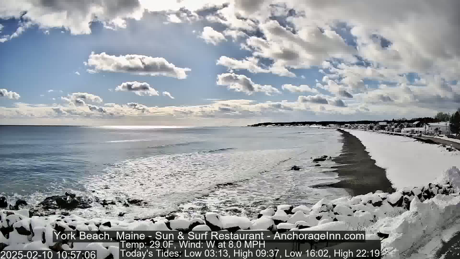 A snow-covered beach stretches along a partly cloudy, cold ocean under a mostly sunny sky.