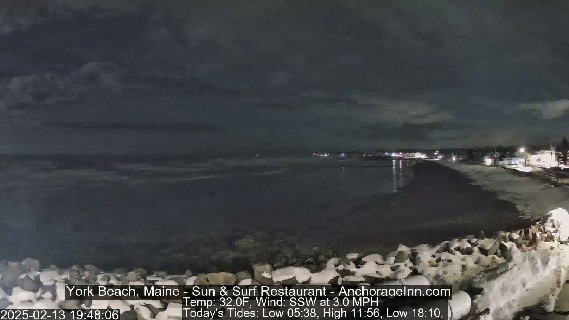 A nighttime view of a snow-dusted beach and calm ocean under a cloudy sky.