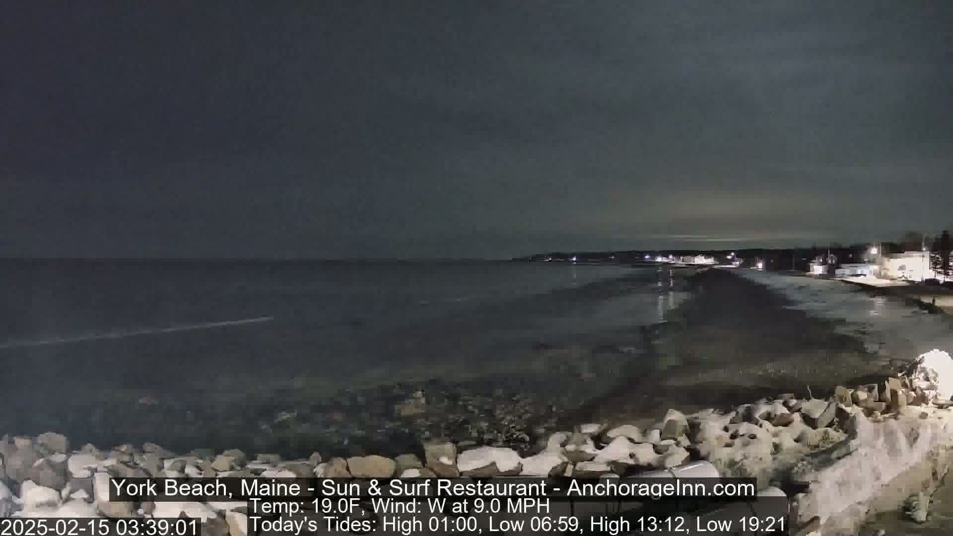 A nighttime view of a rocky shoreline and calm ocean under a dark sky.