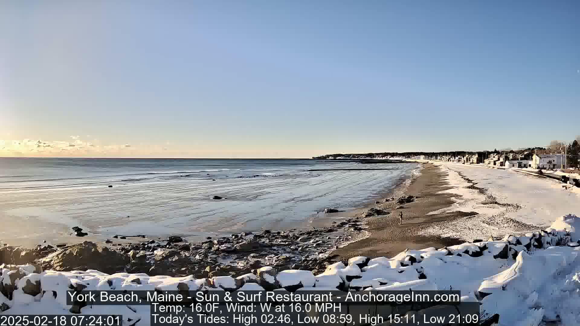 A snow-dusted beach with a calm ocean under a clear, bright sky.