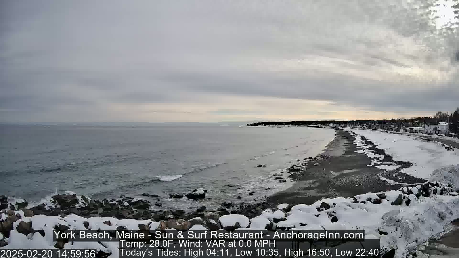 A snow-covered rocky shoreline meets a calm, gray ocean under an overcast sky.