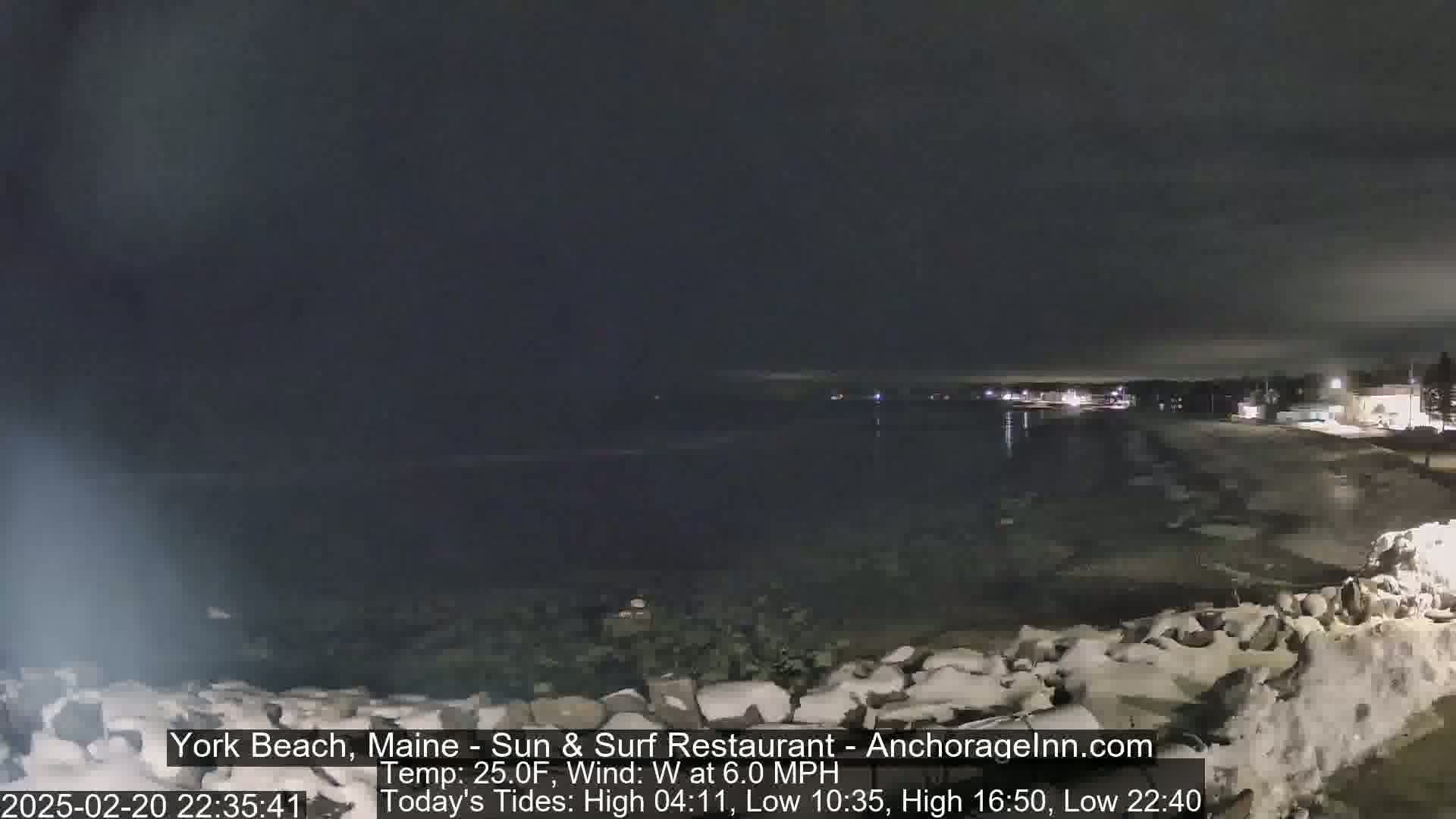 A nighttime view of a dark, icy beach with a calm body of water under a cloudy sky.