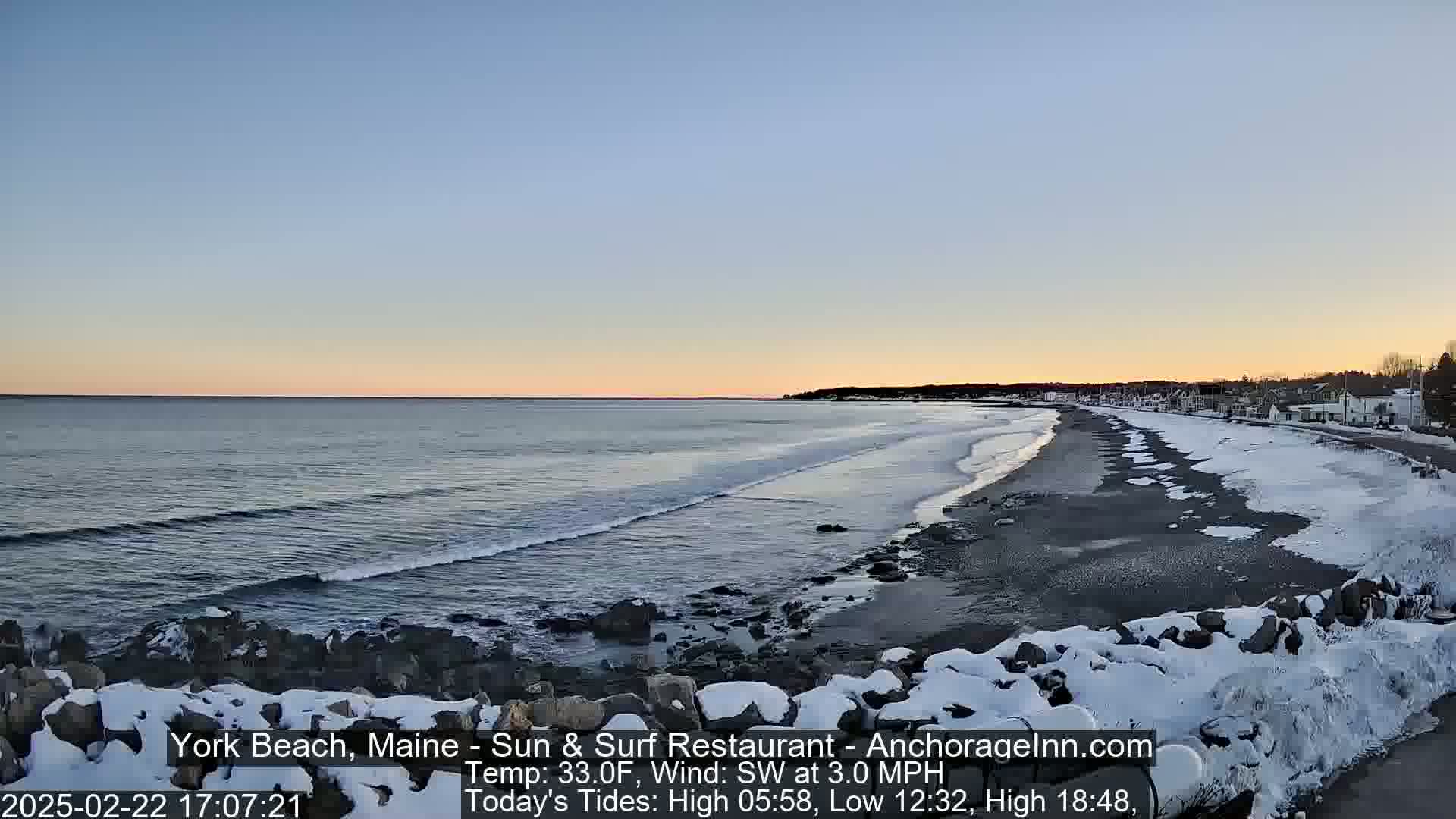 A snow-dusted beach stretches along a calm ocean under a clear, twilight sky.