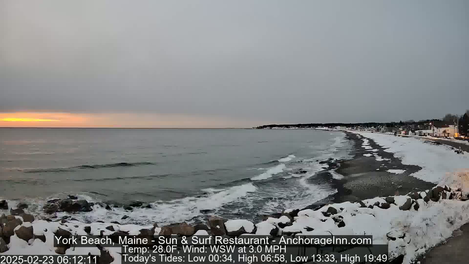 A snowy beach with a calm ocean and a pale sunrise is visible, with a town in the distance.