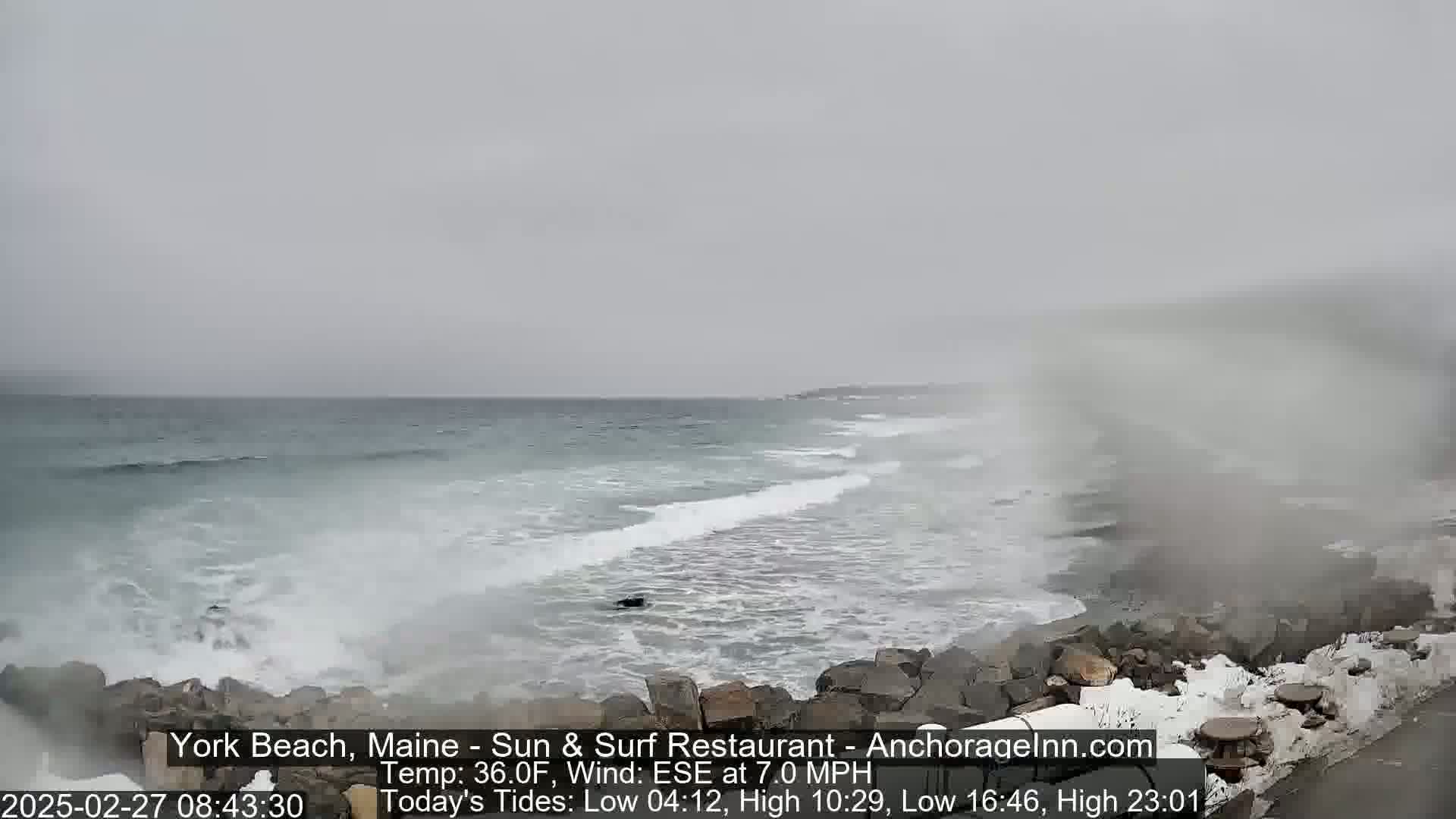 Waves crash against a rocky shoreline on an overcast day.