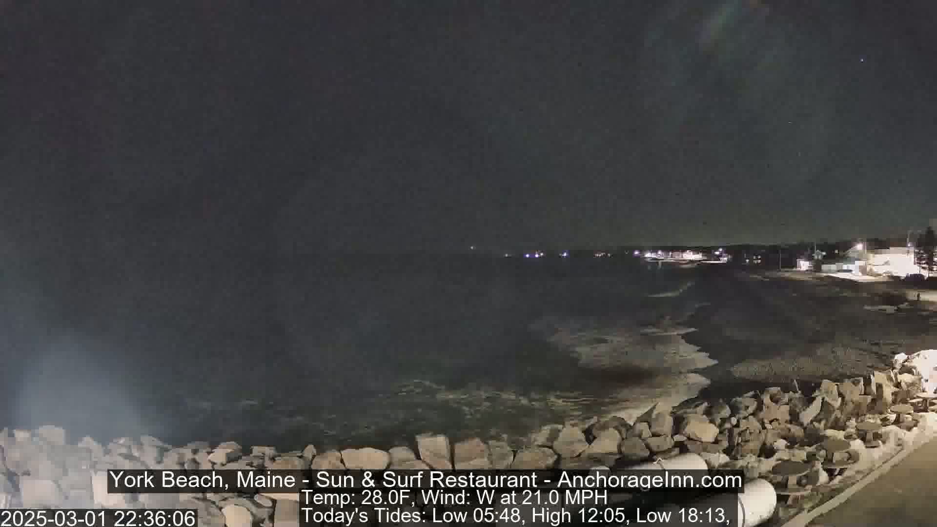 A nighttime view of a rocky shoreline with dark water and waves, under a dark sky.