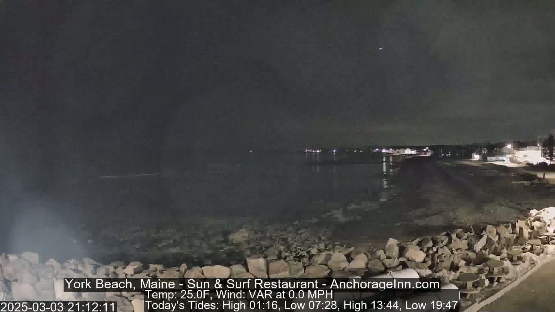 A nighttime view of a rocky shoreline and calm ocean under a dark sky.