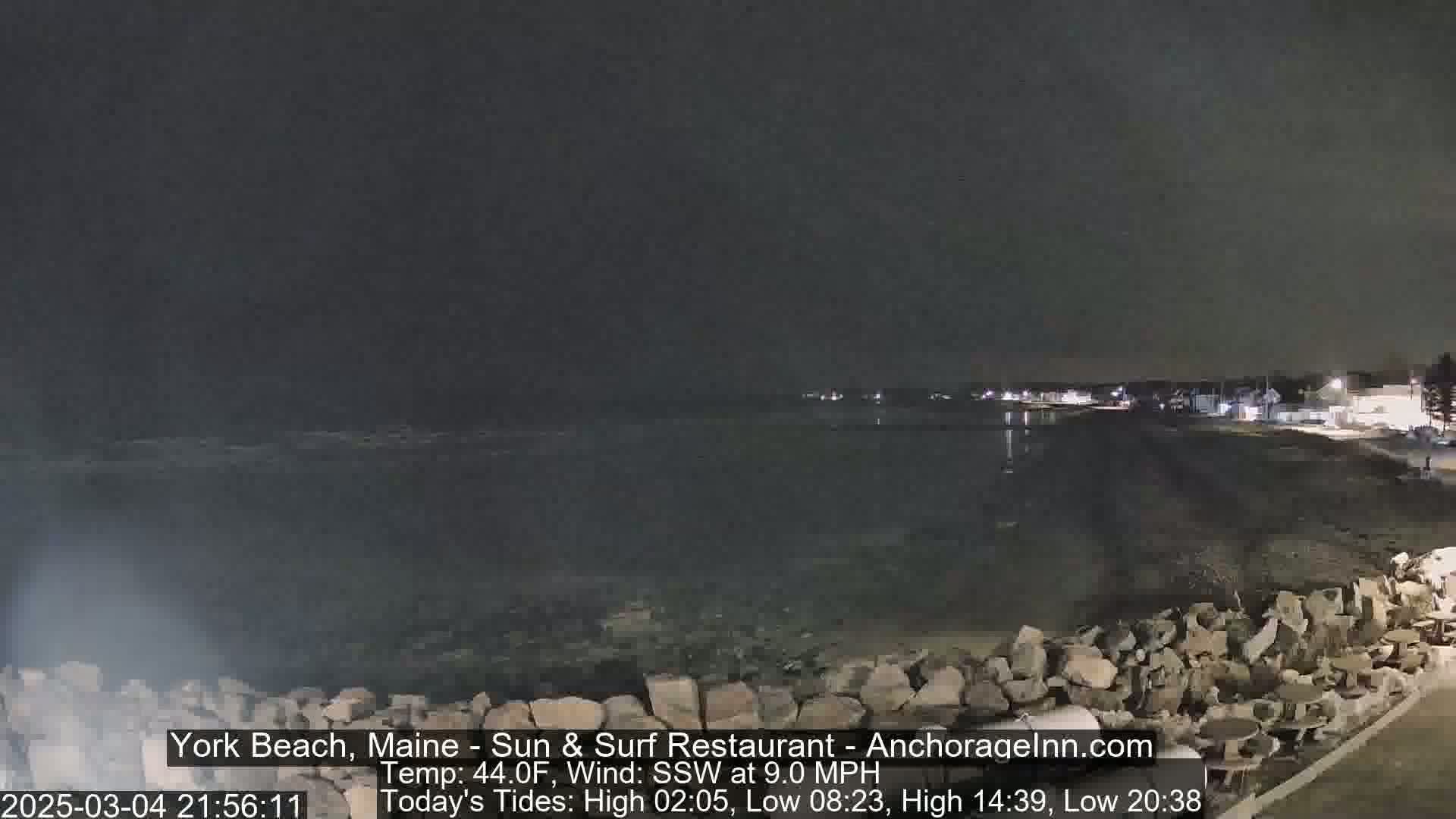 A nighttime view of a rocky shoreline and calm water under a dark sky.
