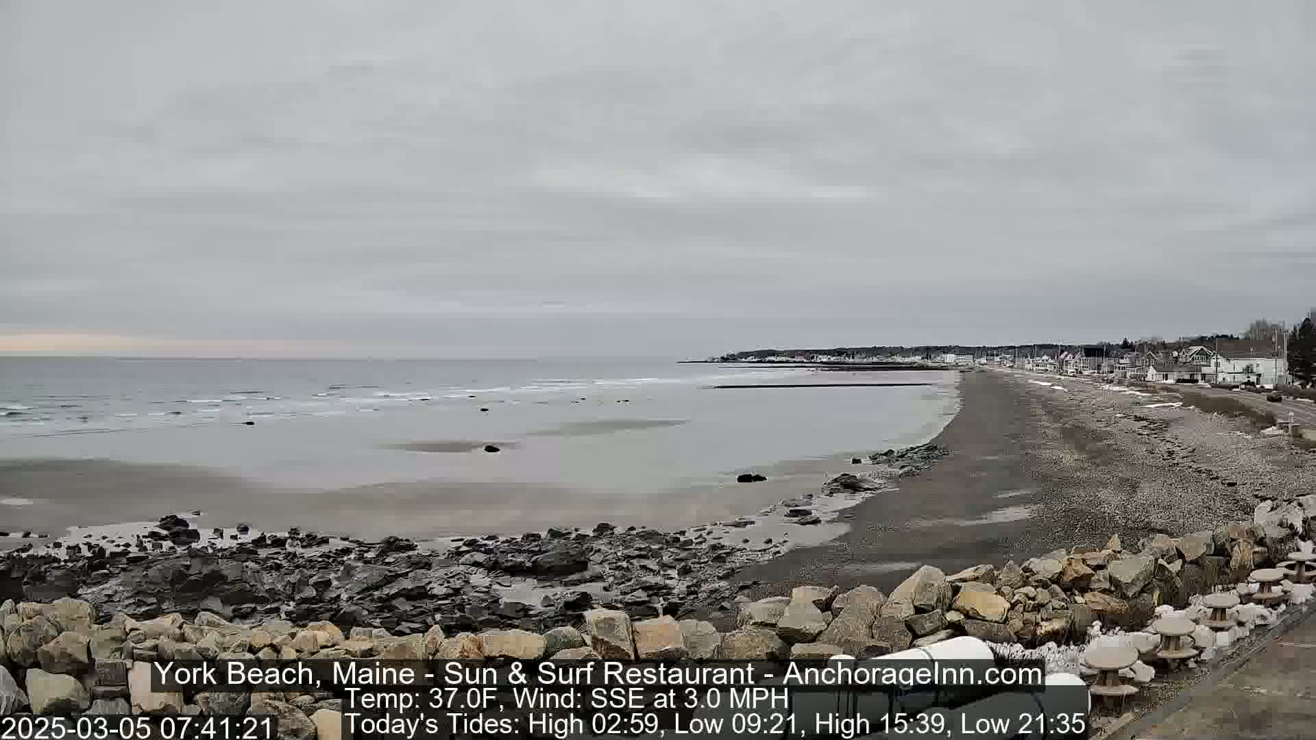 A rocky beach stretches along a calm, grey sea under an overcast sky.