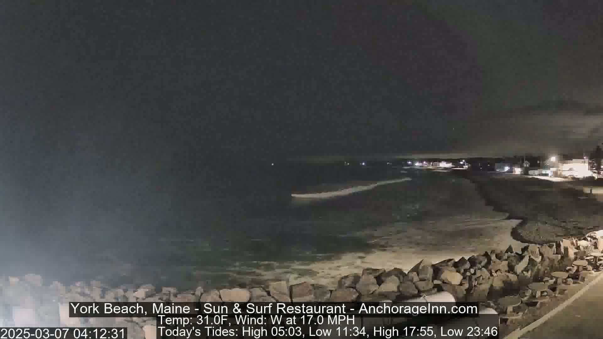 A nighttime view of a rocky shoreline and ocean under a dark sky with a 17 mph westerly wind.