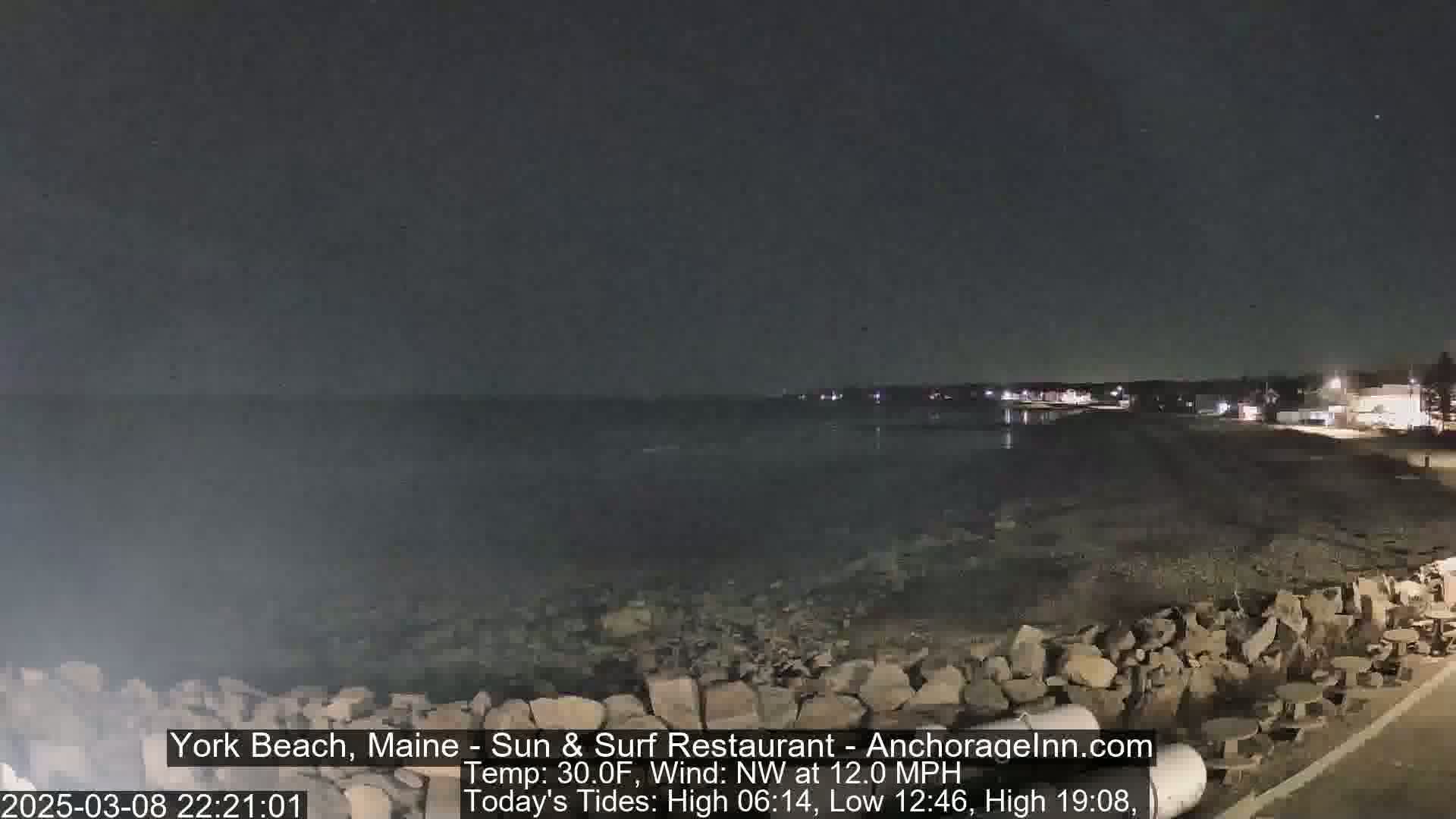 A nighttime view of a rocky shoreline and calm ocean under a dark sky.
