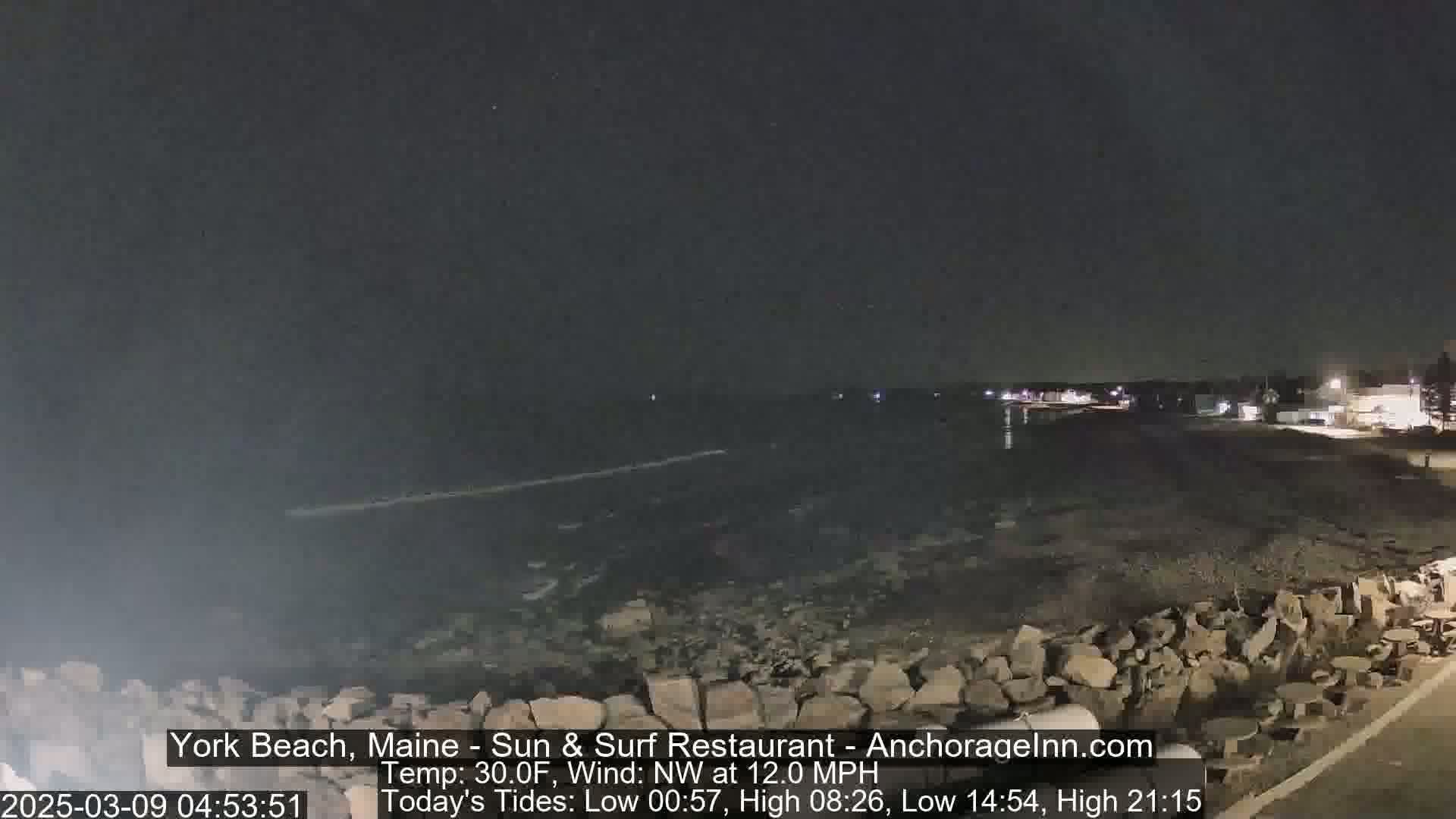 A nighttime view of a rocky shoreline and dark ocean under a clear, starlit sky.