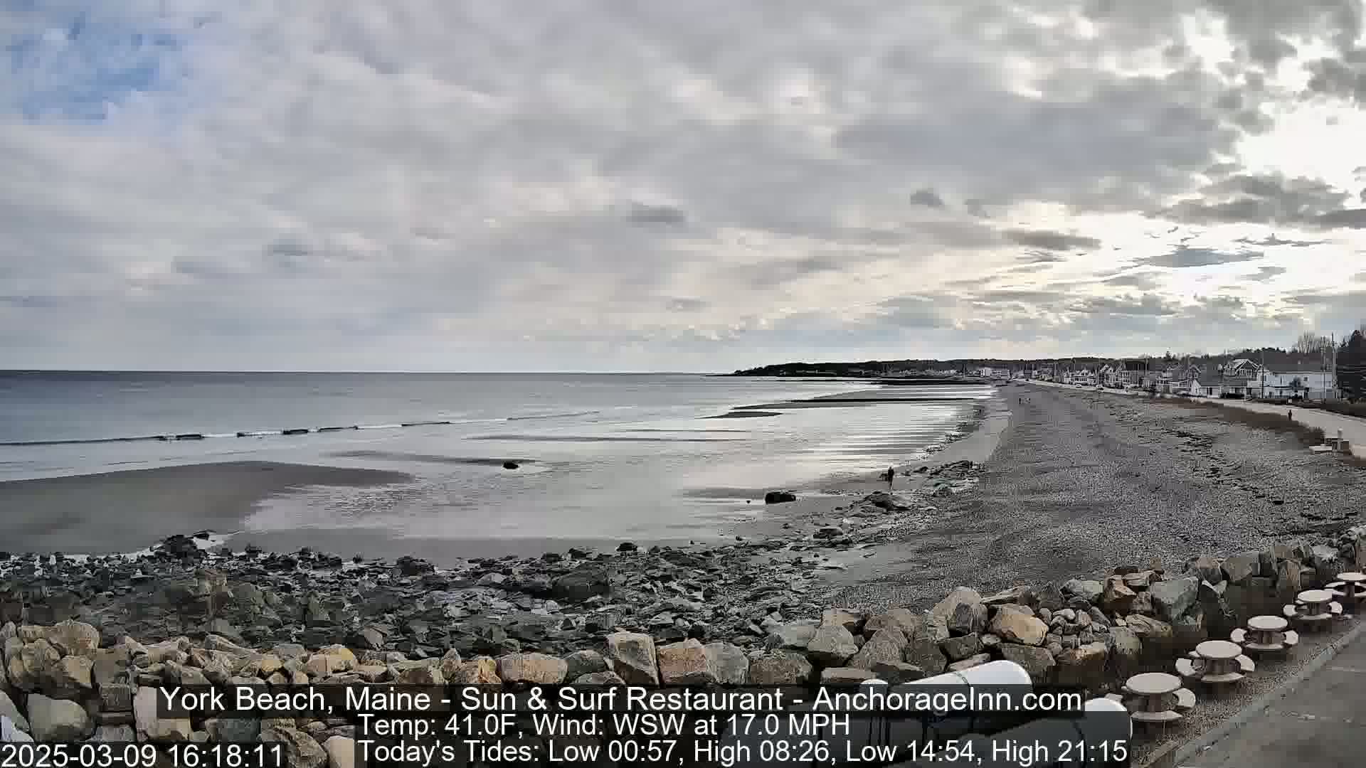A rocky beach stretches out to a calm ocean under a cloudy sky.
