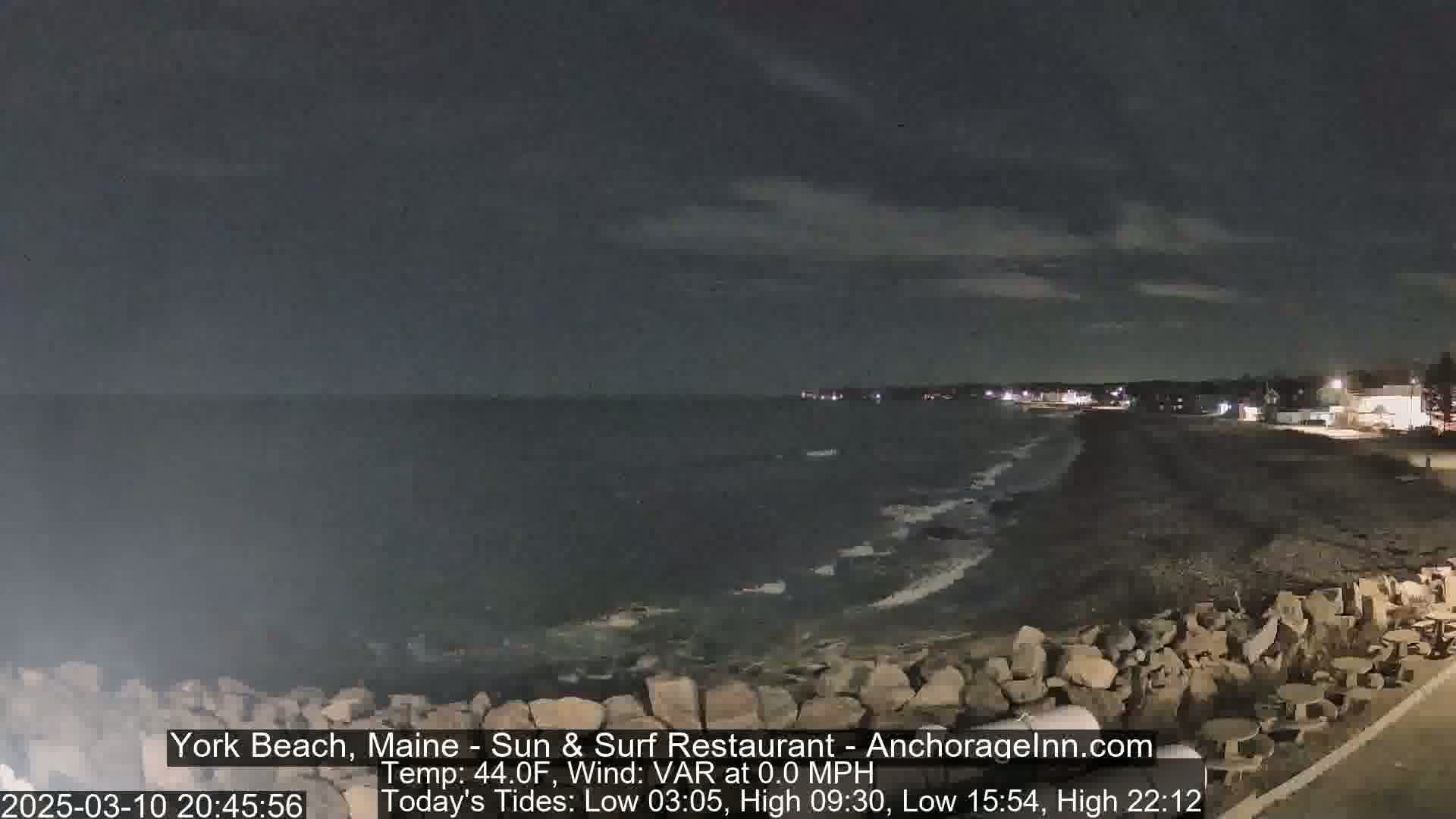 A nighttime view of a rocky shoreline with a calm ocean under a dark, cloudy sky.