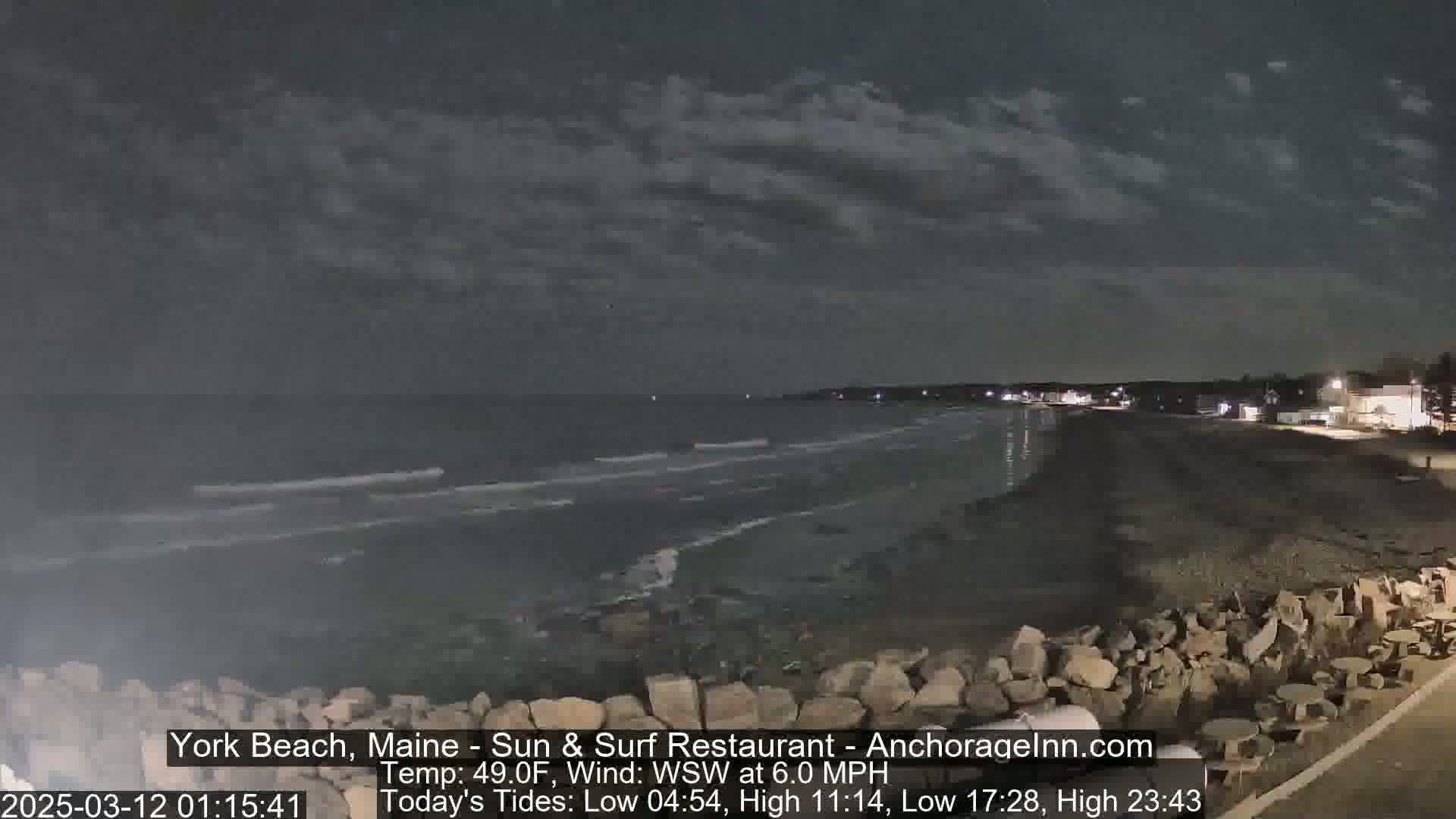 A dark, nighttime beach scene shows a calm ocean under a cloudy sky.