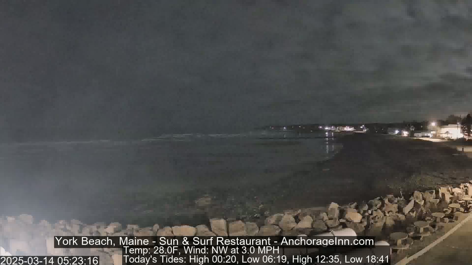 A dark, nighttime beach scene with a calm ocean under a cloudy sky.