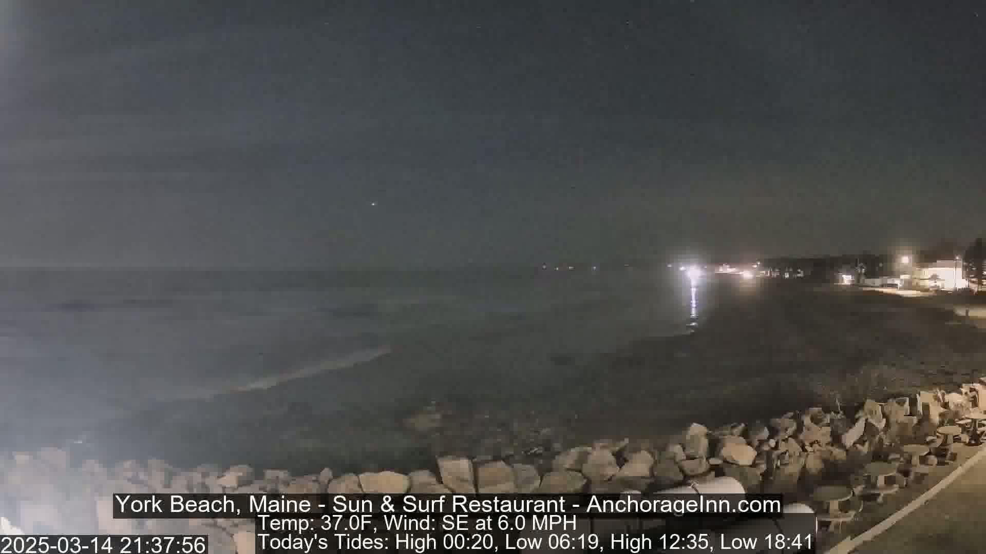 A nighttime view of a rocky beach with a calm ocean under a dark sky.