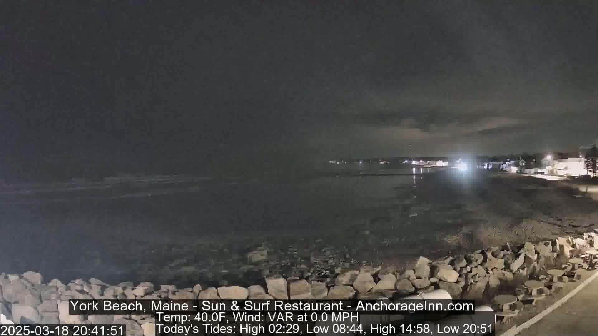 A nighttime view of a rocky shoreline and calm ocean under a dark sky.
