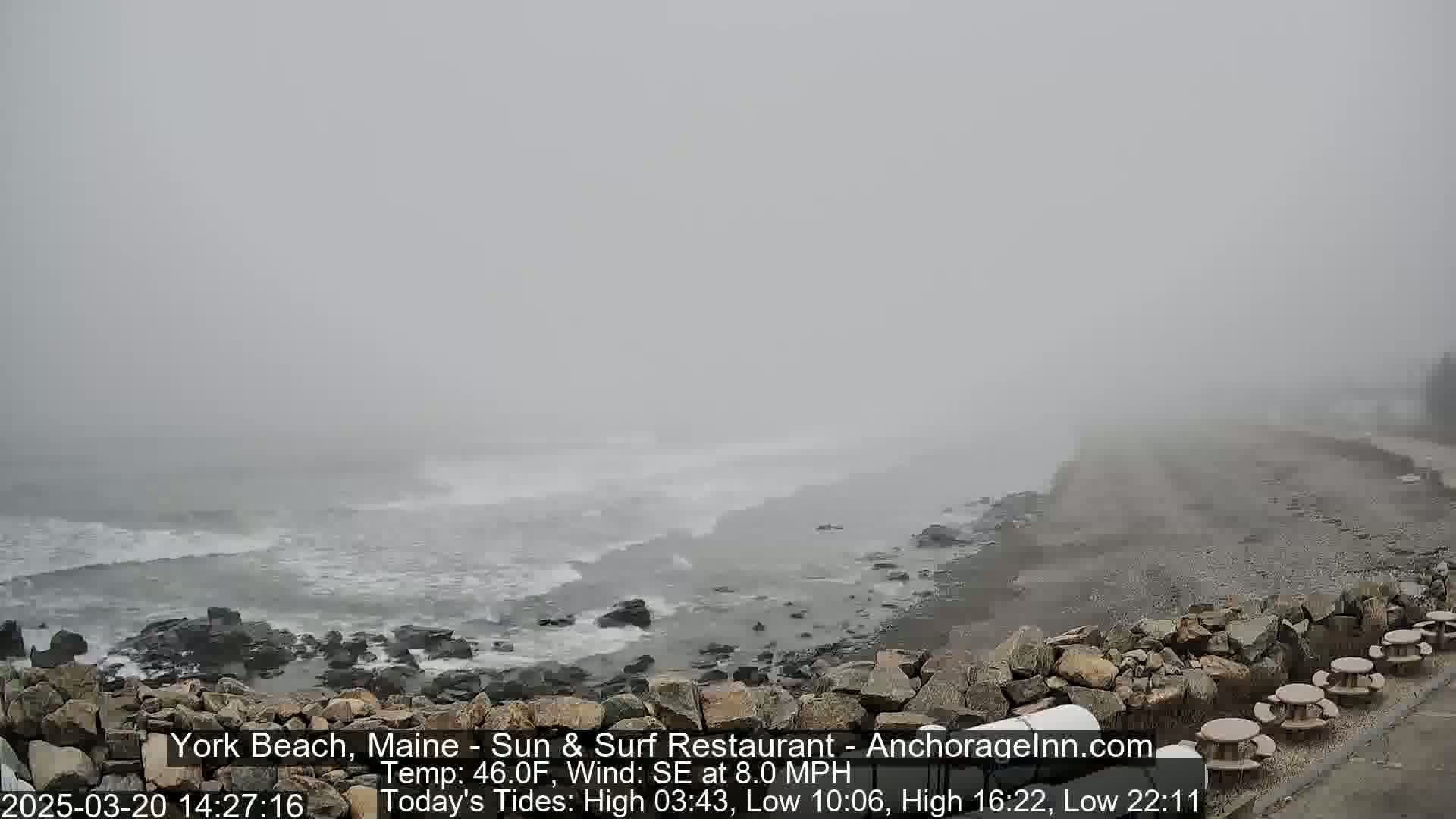 A foggy coastline shows a rocky shore with choppy waves in the ocean.