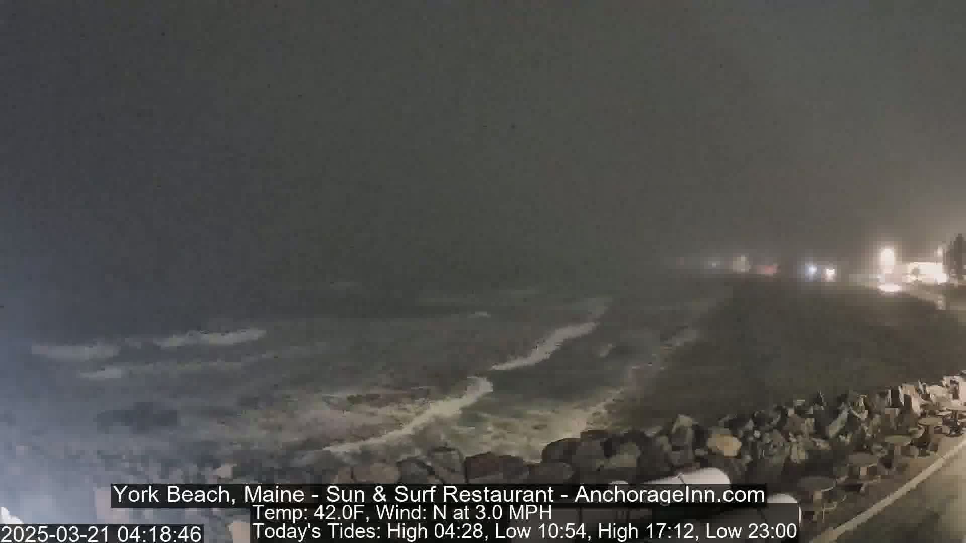 Dark, stormy waves crash against a rocky shoreline under a foggy, nighttime sky.