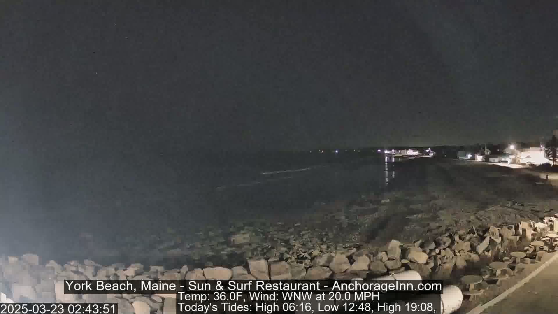 A nighttime view of a rocky shoreline and dark ocean under a clear, dark sky with a 20 mph wind.