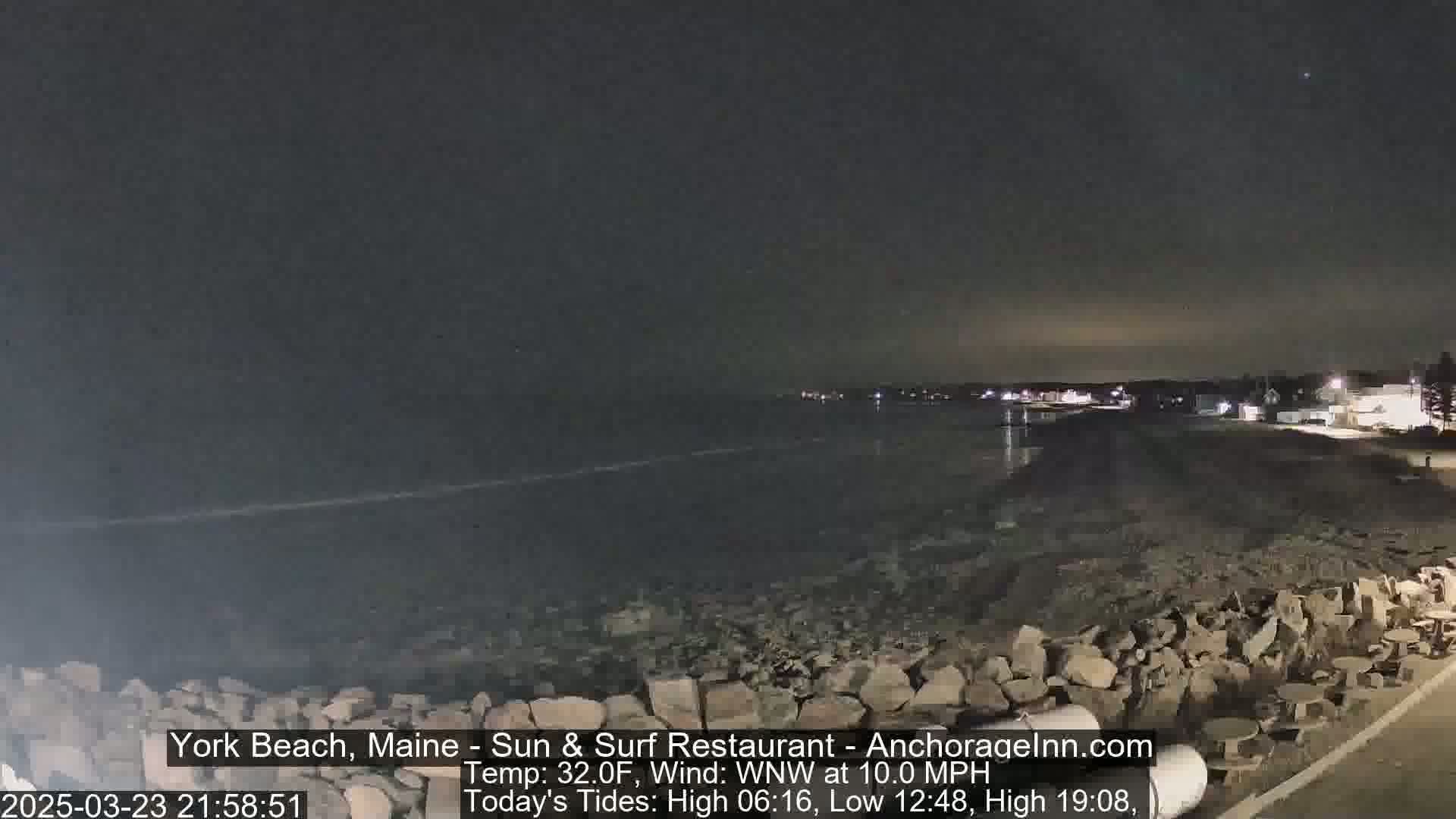 A nighttime view of a rocky shoreline and calm ocean under a dark sky.