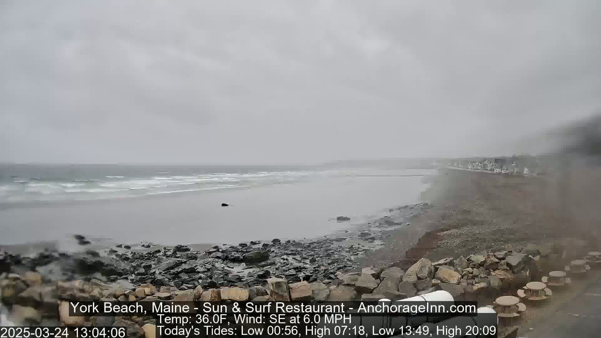 A rocky beach with a gray, overcast sky and a choppy ocean under a light drizzle.