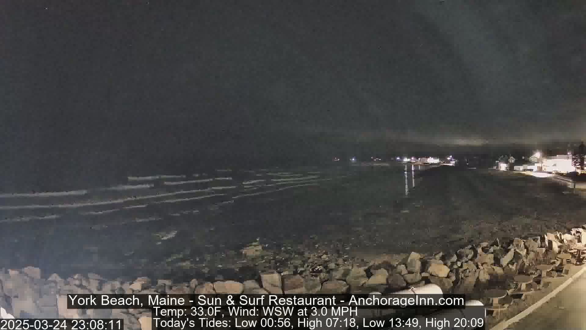 A nighttime view of a rocky shoreline with gently lapping waves under a dark sky.